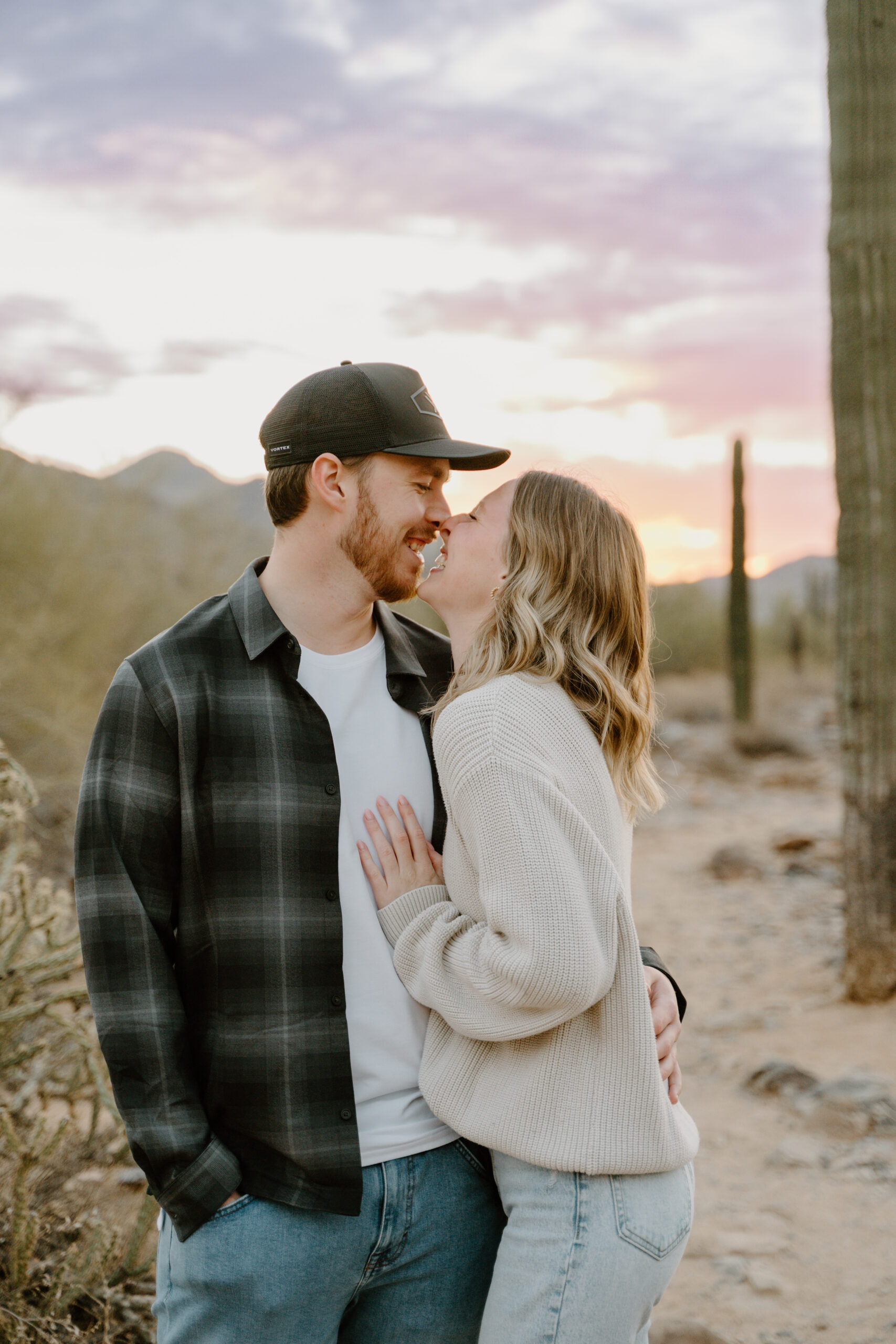 A candid moment of a couple laughing together at sunset, with towering saguaros in the background, highlighting the golden glow of Arizona engagement session locations.