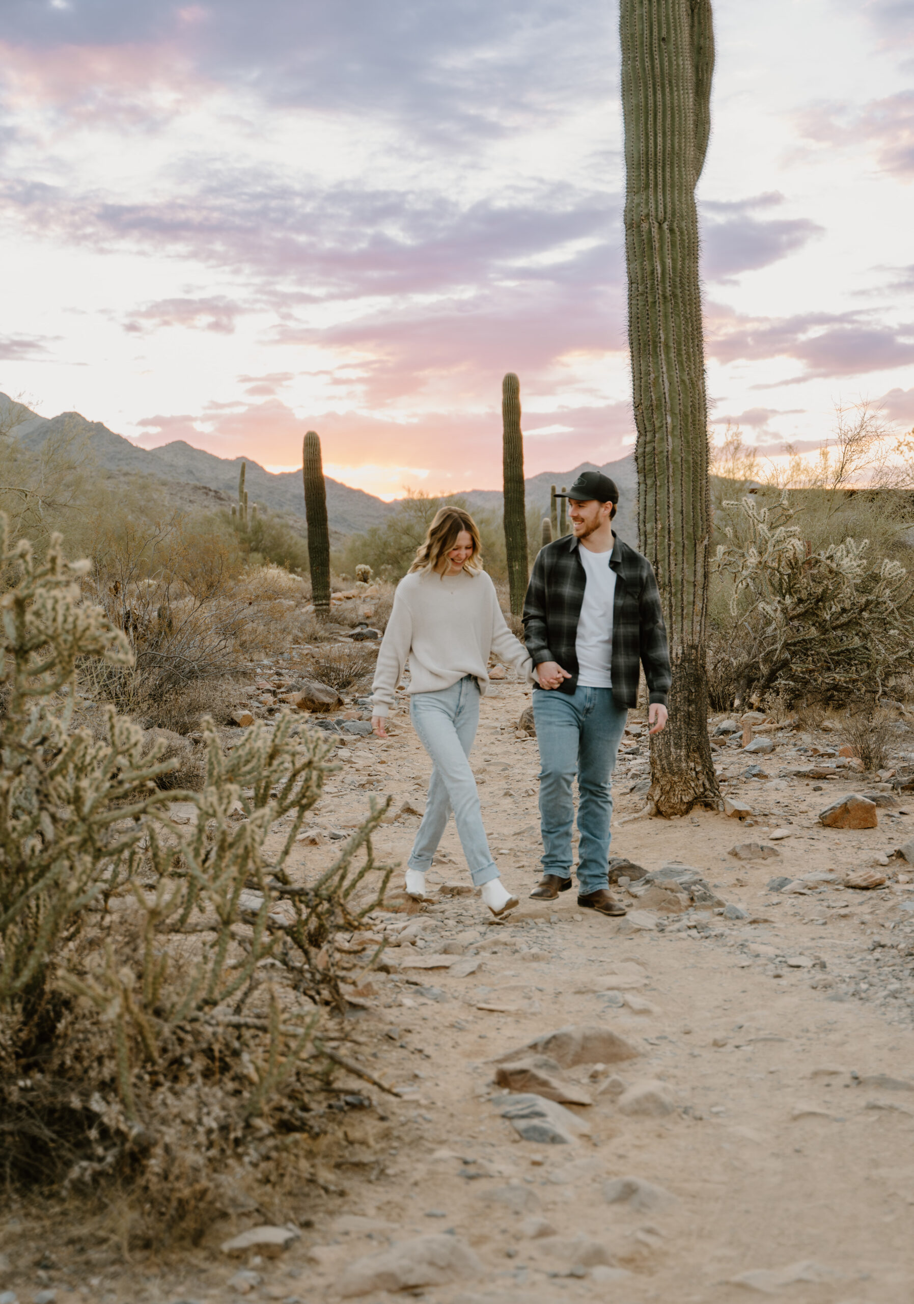 A romantic scene with a couple standing together in the desert at sunset, with soft pink and blue hues in the sky, showing the dreamy lighting at Arizona engagement session locations.