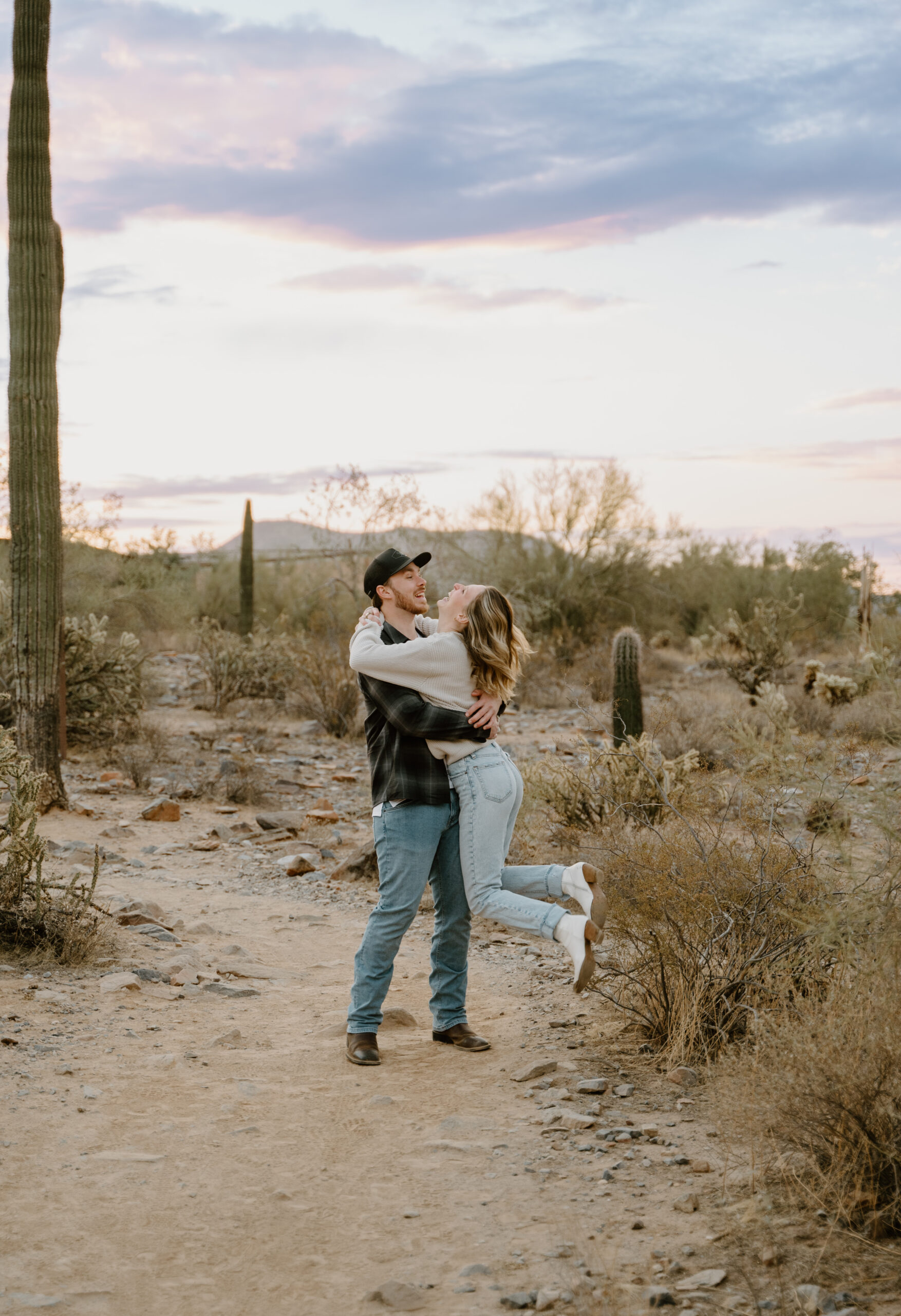 A playful engagement session moment, laughing together in a scenic Arizona engagement session location with desert plants and open space.