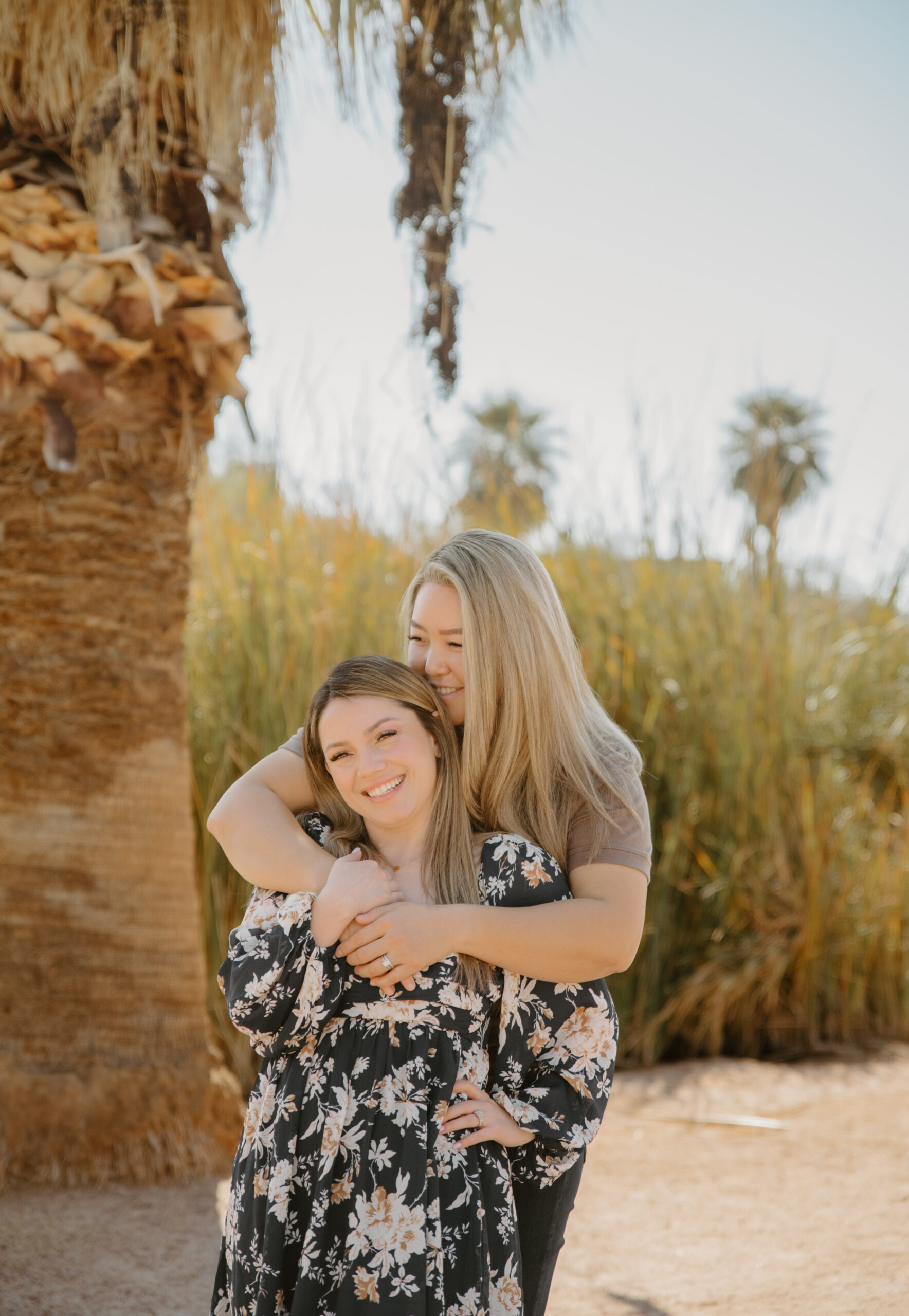 A couple stands near a pond lined with palm trees, creating a unique and picturesque engagement session location in Arizona that blends desert and tropical elements.