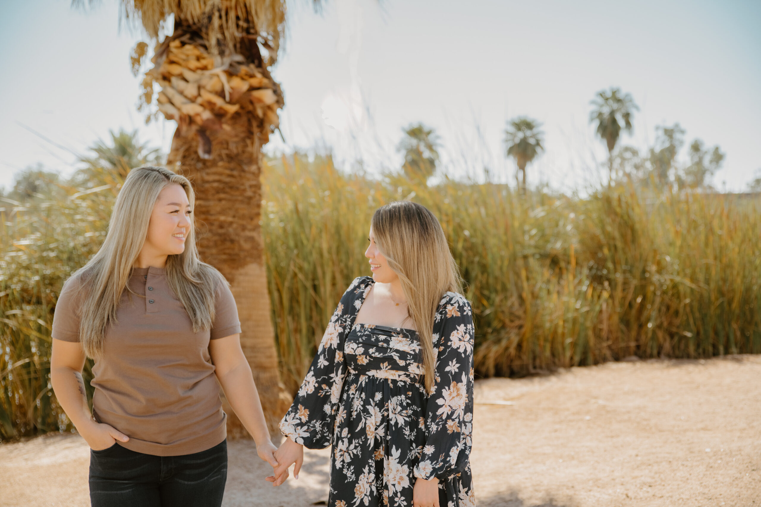 A couple stands near a pond lined with palm trees, creating a unique and picturesque engagement session location in Arizona that blends desert and tropical elements.