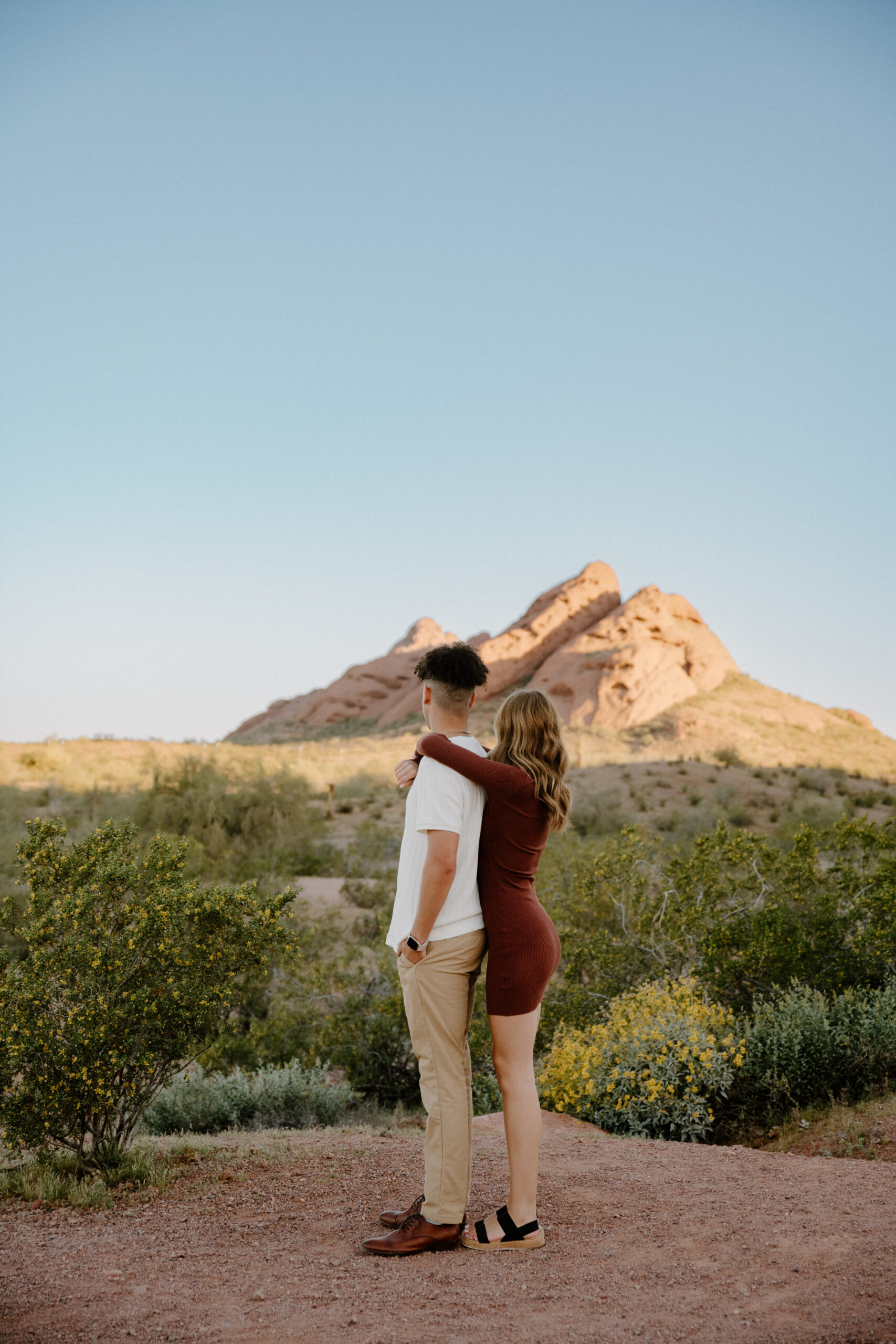 A stylish couple poses in front of Papago Park's red rock formations and palm trees, showcasing one of the most diverse and scenic Arizona engagement session locations.