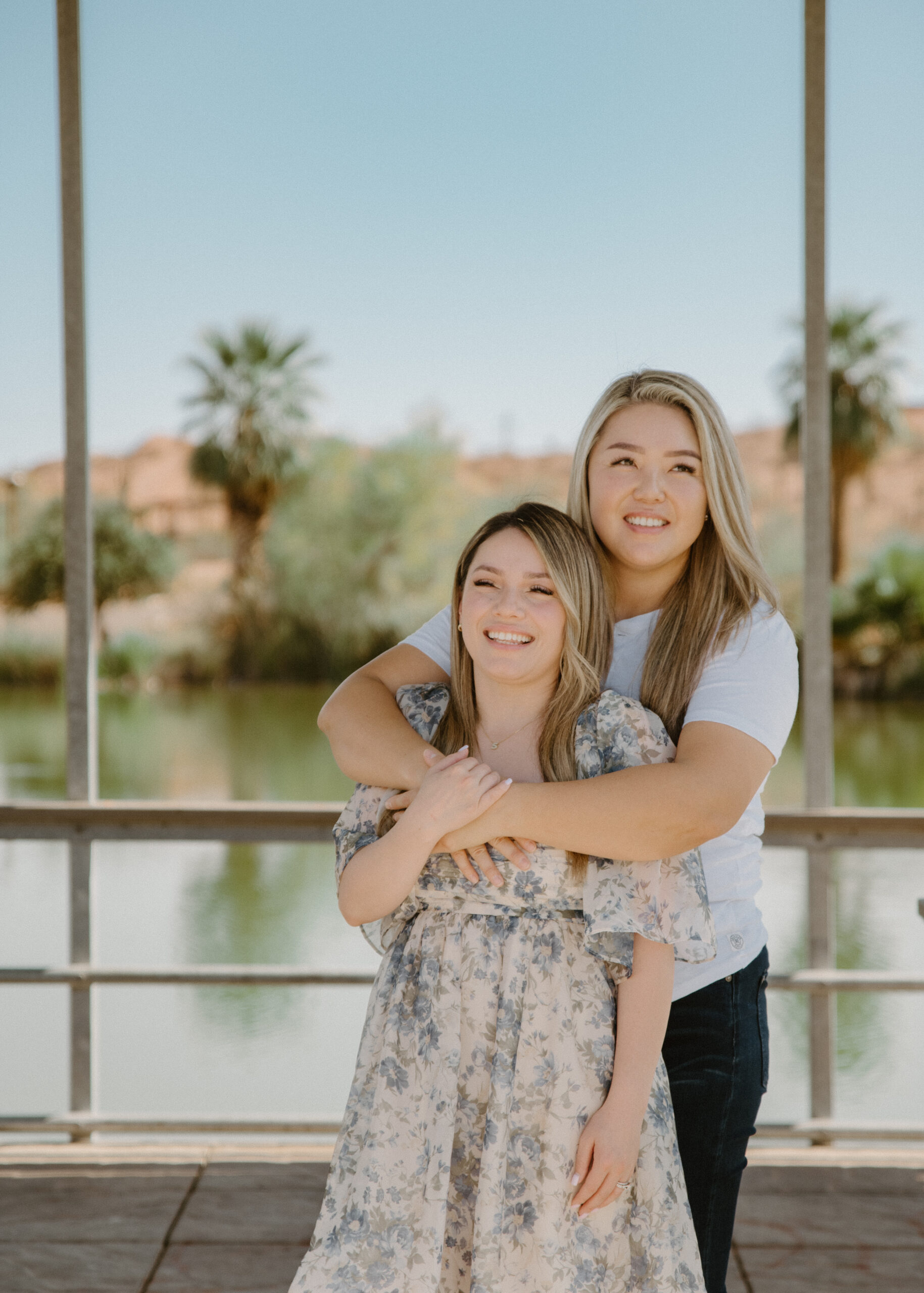 A couple stands near a pond lined with palm trees, creating a unique and picturesque engagement session location in Arizona that blends desert and tropical elements.