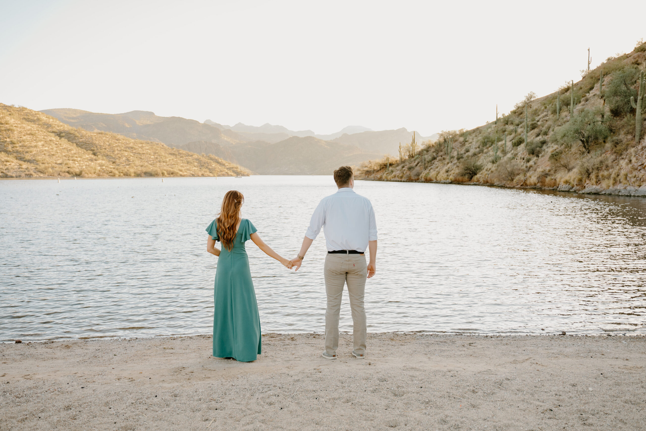 Couple holding hands facing Saguaro Lake during sunset