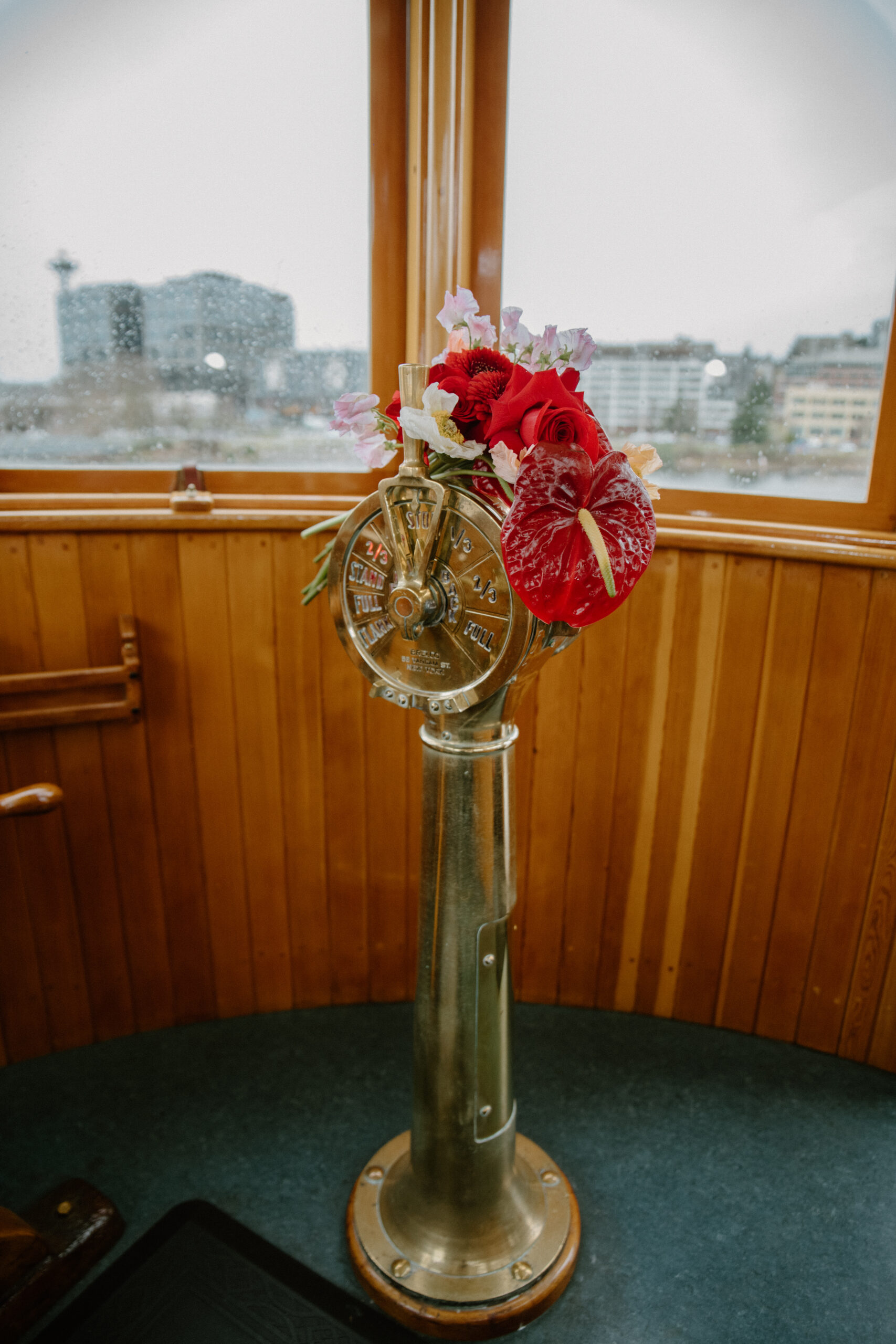 Red and pink floral bouquet placed on the classic ship wheel, perfect decor for an intimate boat wedding at a Virginia wedding venue.