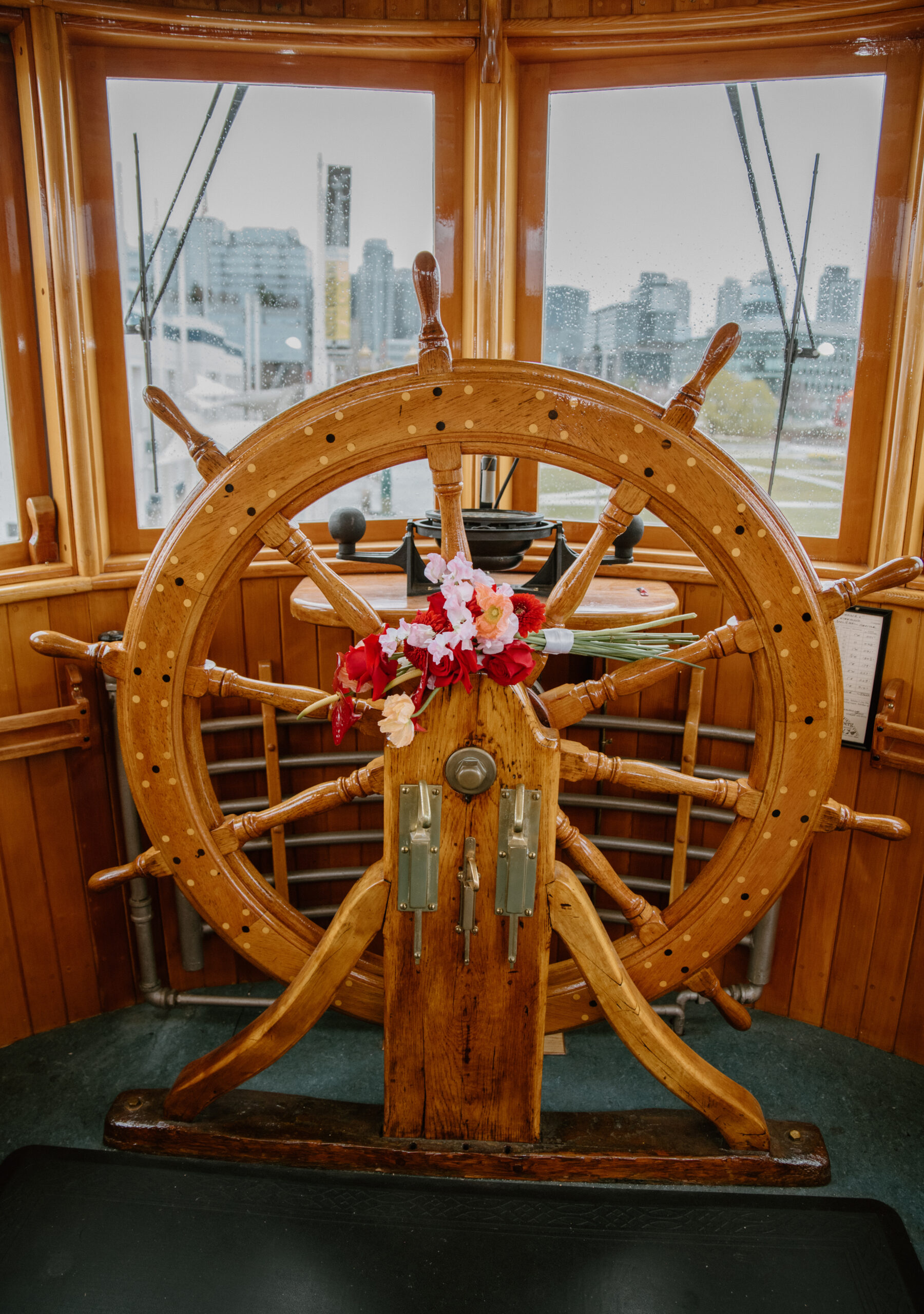 Red and pink floral bouquet placed on the classic ship wheel, perfect decor for an intimate boat wedding at a Virginia wedding venue