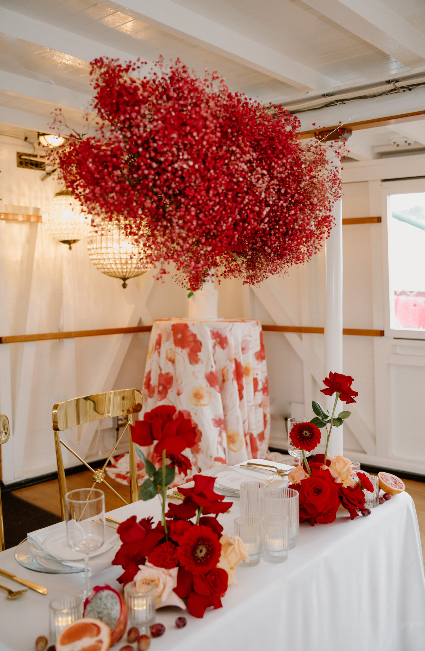 Reception table with bold red floral arrangements and a hanging cloud of baby's breath flowers on the boat wedding ship.