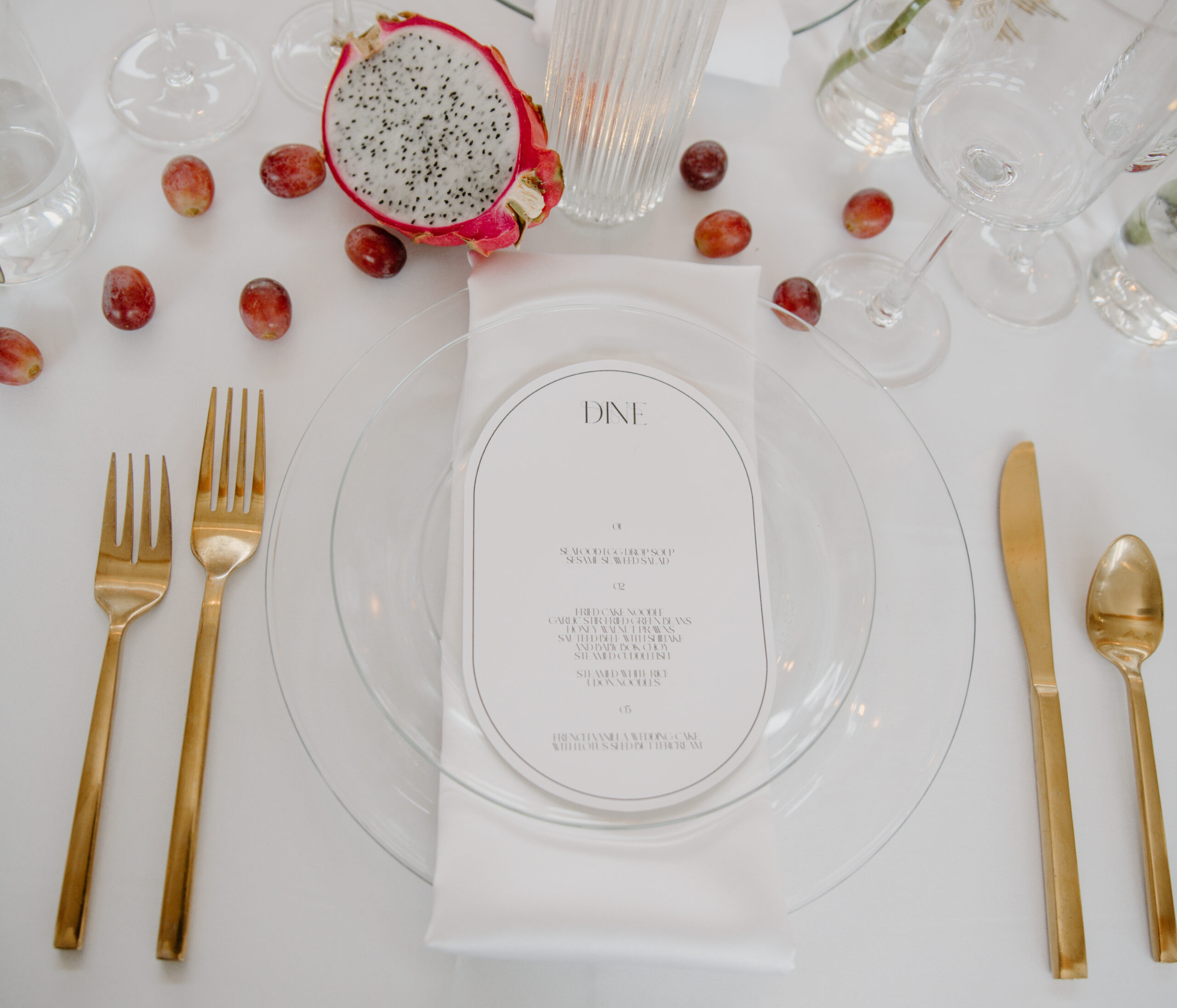 Flat lay of modern wedding menu with gold flatware and dragon fruit details during boat wedding reception. 