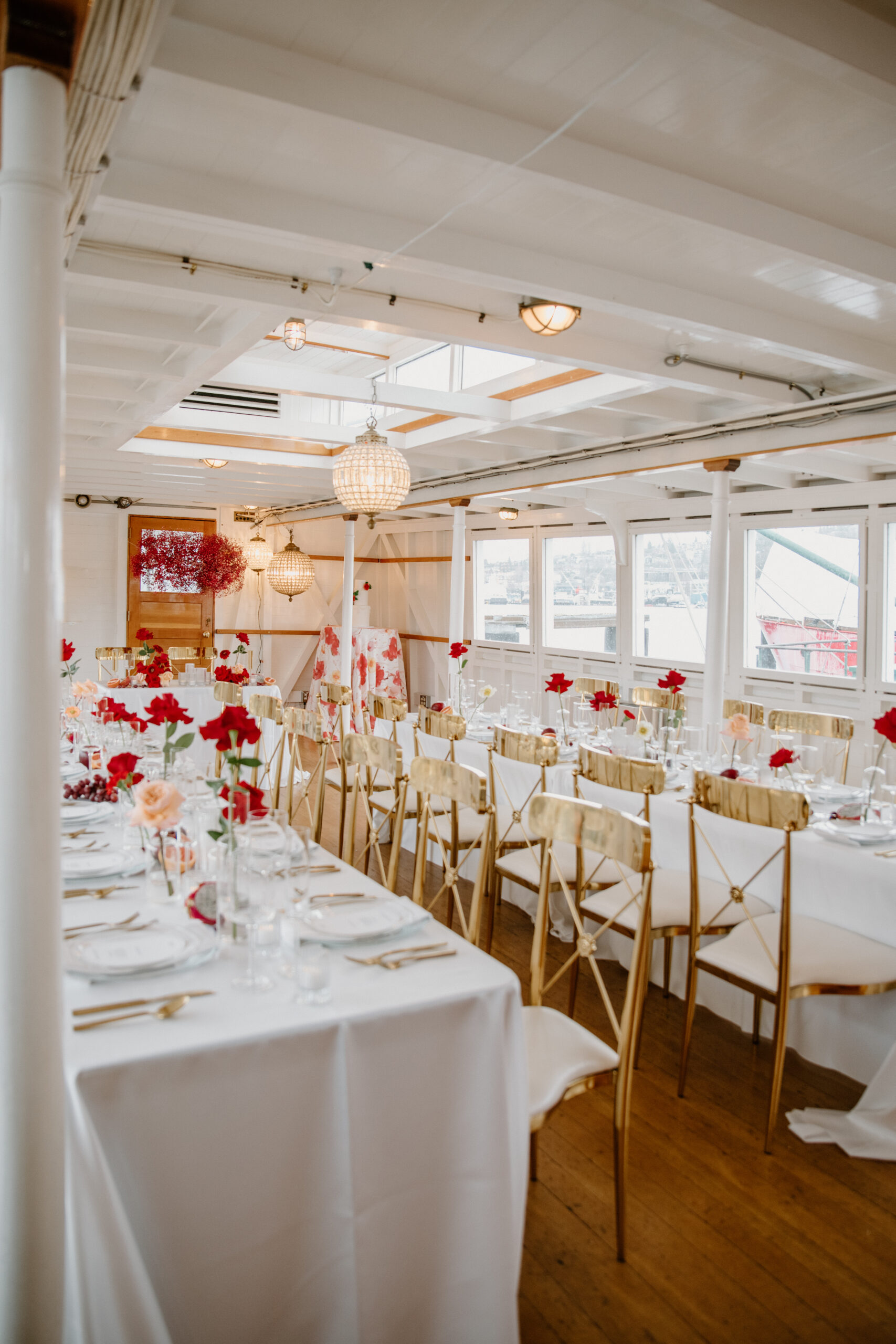 Reception table with bold red floral arrangements and a hanging cloud of baby's breath flowers on the boat wedding ship.