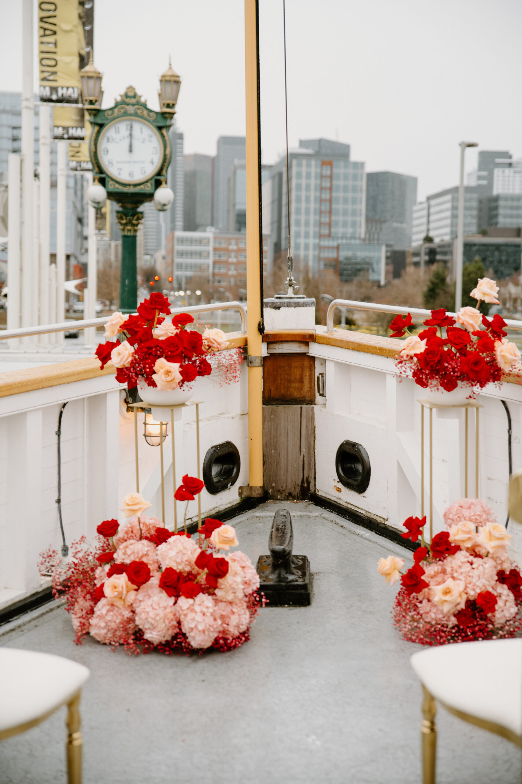 View of the boat wedding reception deck, with rows of tables adorned with red florals and gold chairs.