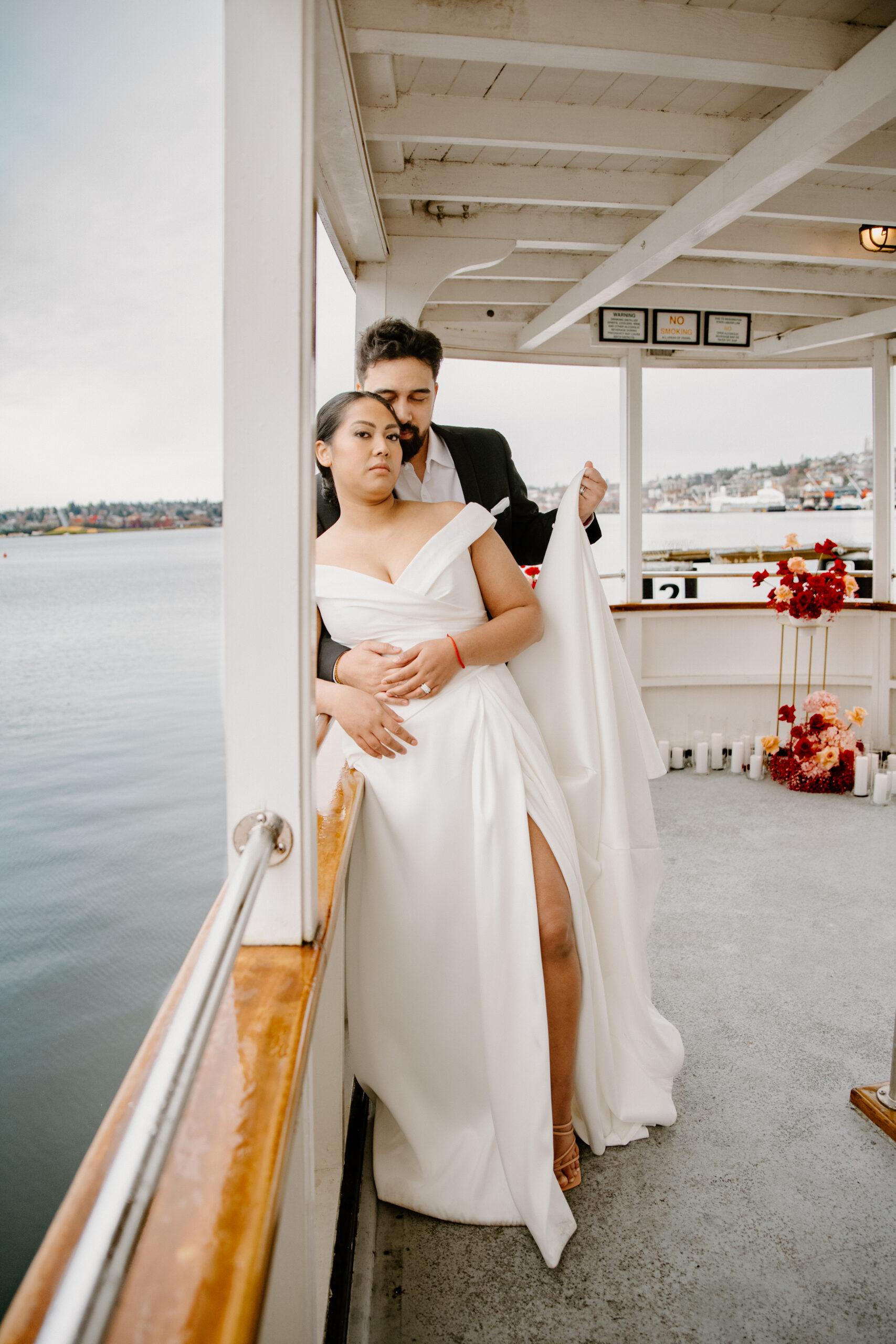 Bride and groom standing on the back deck of the boat, surrounded by romantic red floral arrangements at their boat wedding.