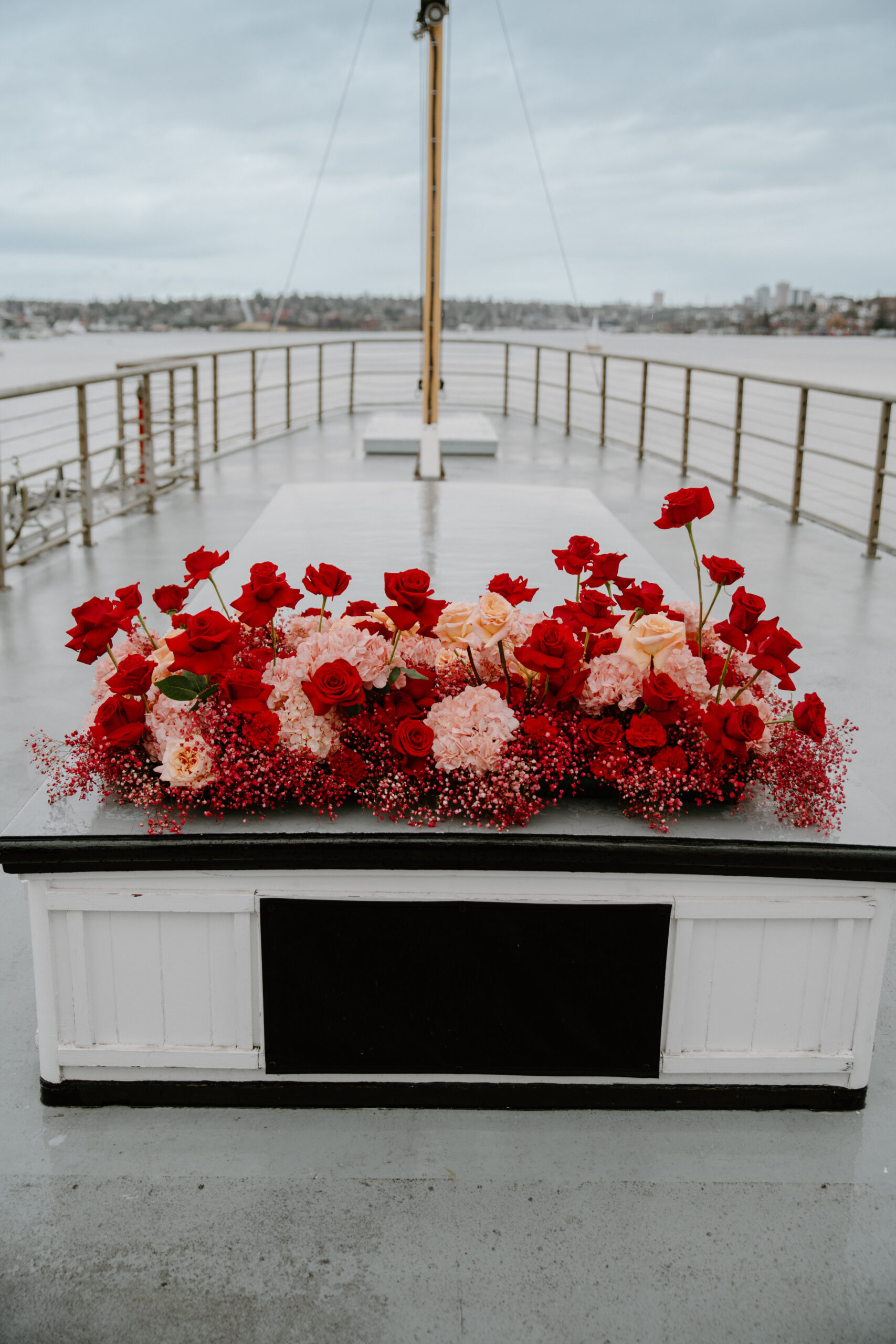 Red and blush floral centerpiece on the deck of a historic boat wedding venue overlooking the water.