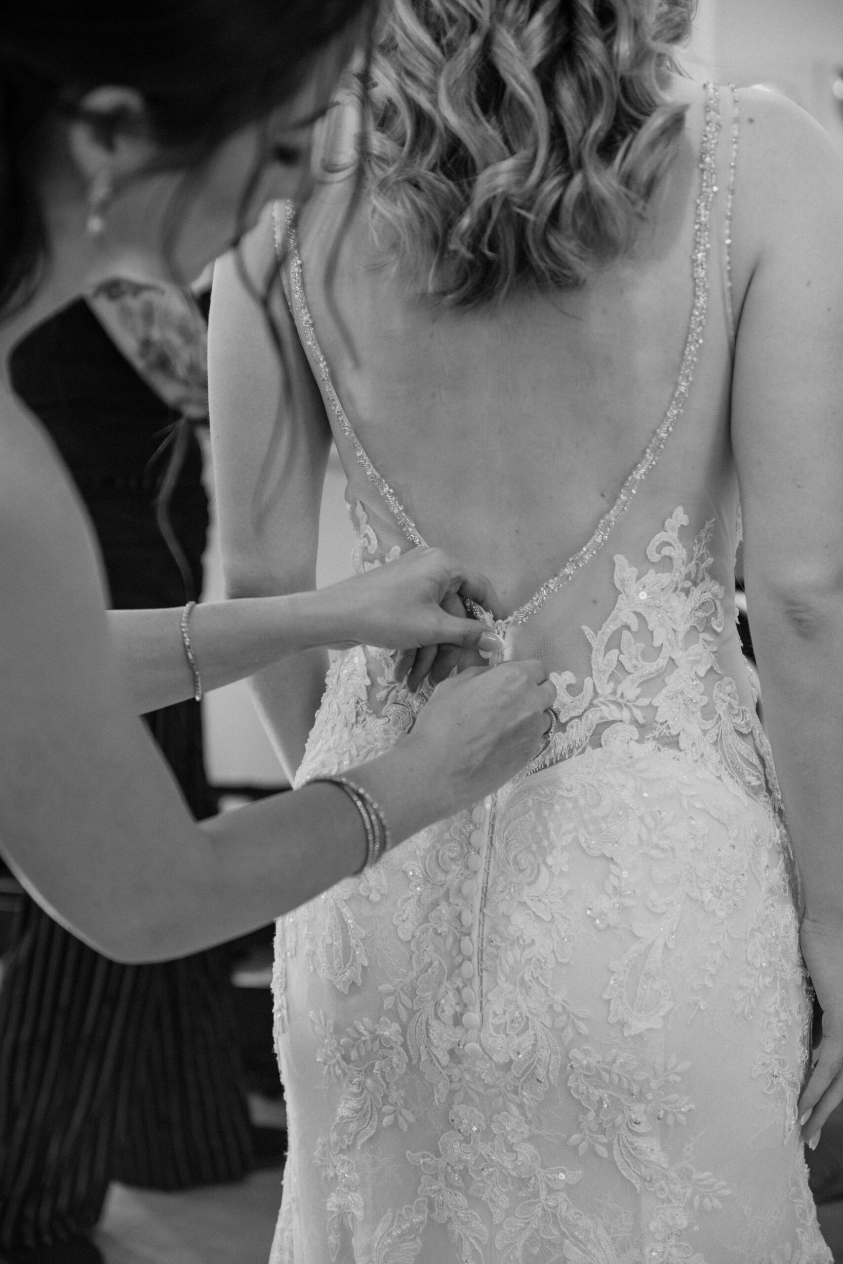 Close-up black and white shot of the bride's dress being buttoned up during the getting ready process.