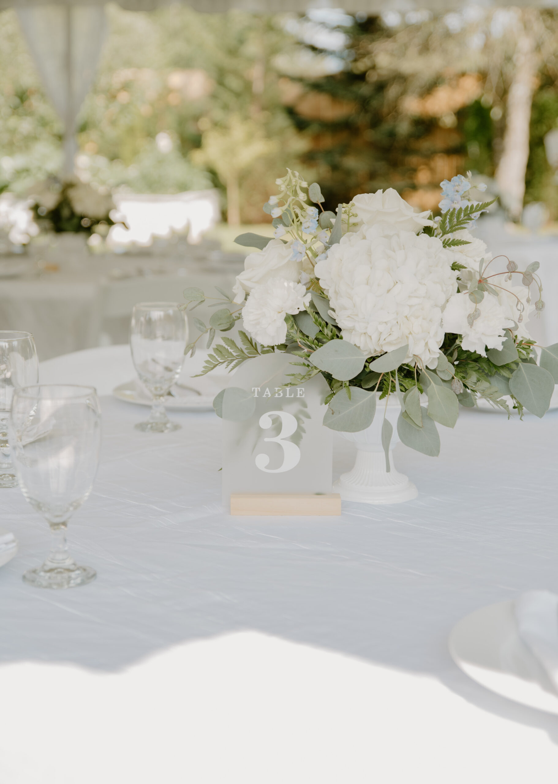 Table centerpiece with white florals and greenery, styled under a tent for a reception at Jackson Manor Events.