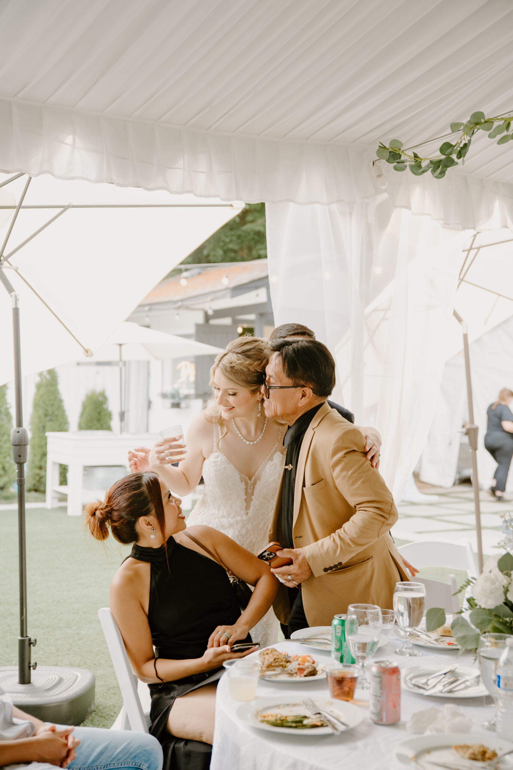 Bride leans in to greet family members during the reception, smiling warmly while interacting with guests at their dinner table.