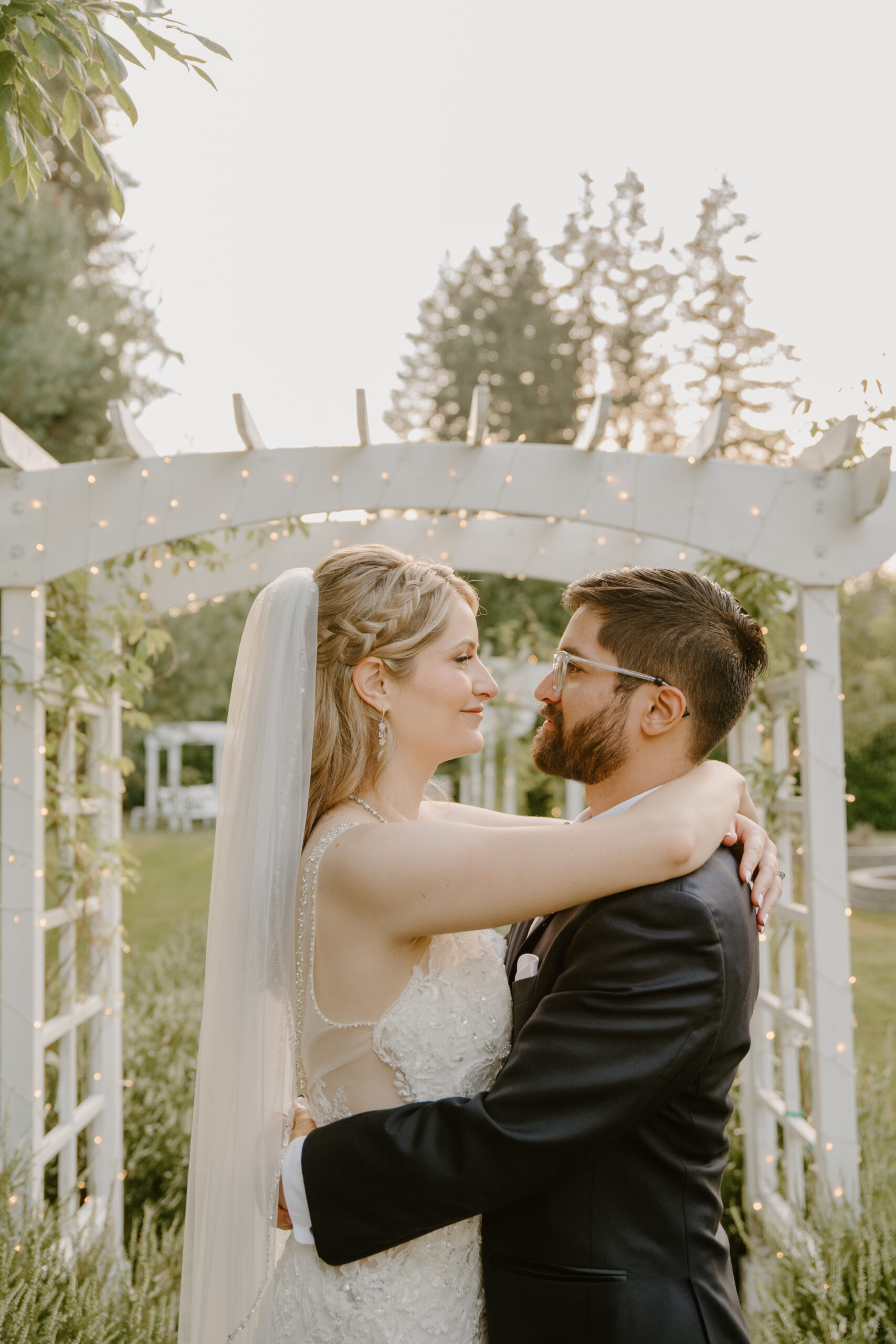 The newlyweds embrace under a softly lit pergola at sunset, surrounded by glowing fairy lights in the romantic garden at Jackson Manor Events.