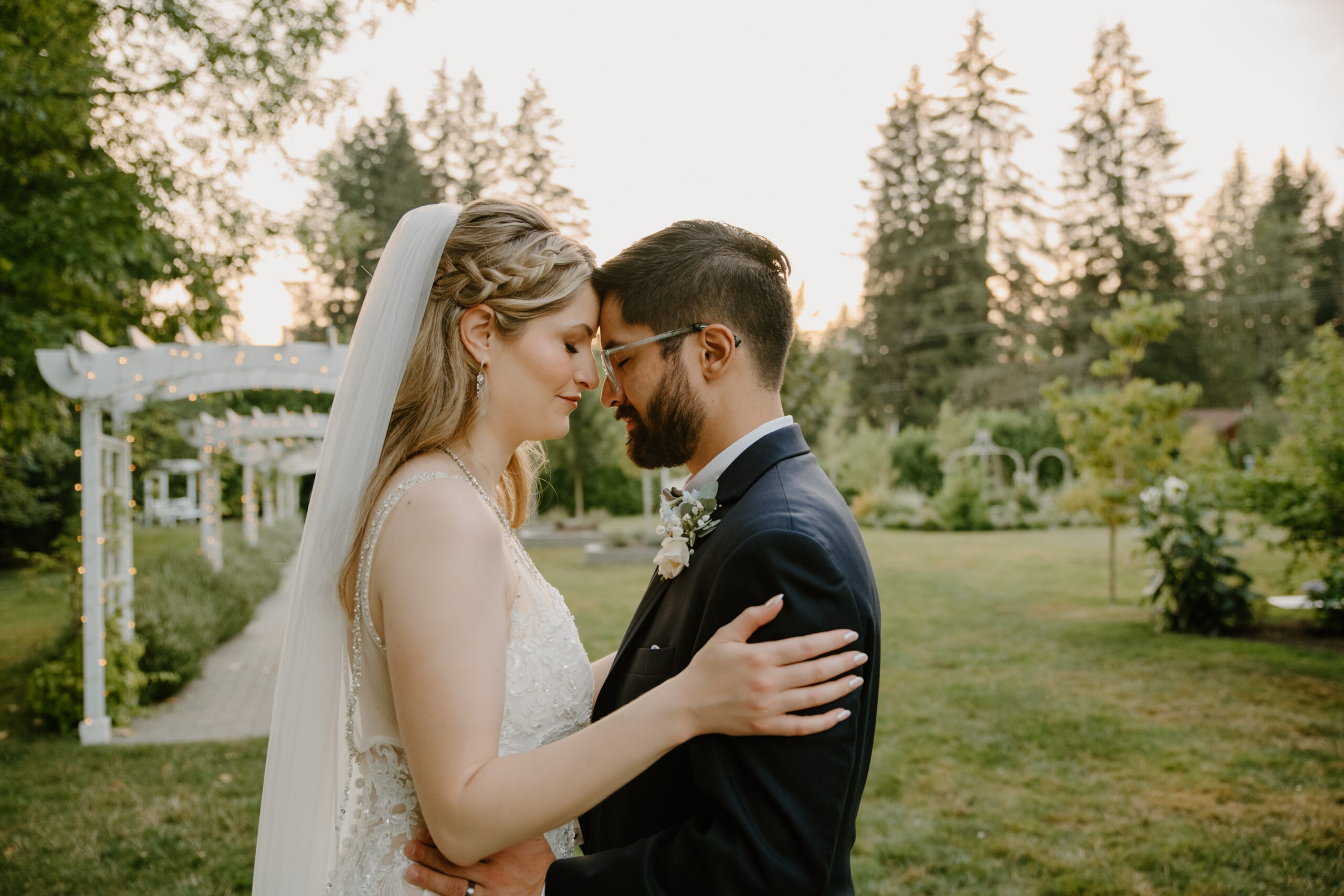 The newlyweds embrace under a softly lit pergola at sunset, surrounded by glowing fairy lights in the romantic garden at Jackson Manor Events.