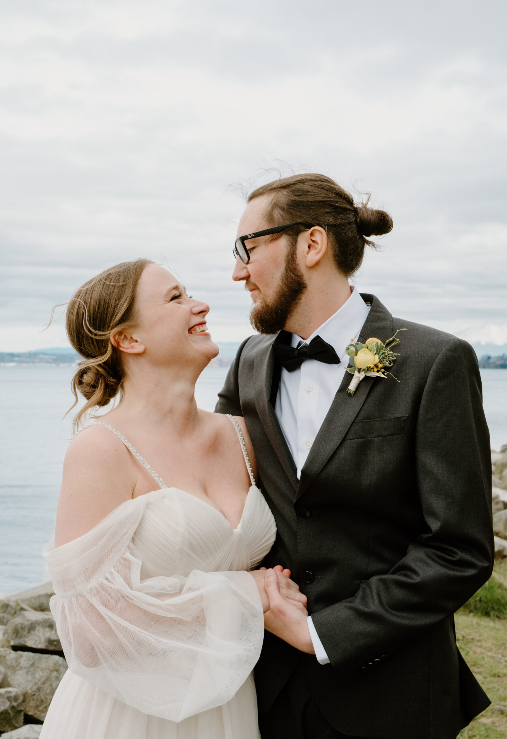 Close-up of a smiling couple looking into each other’s eyes beside the water, capturing the sweet emotions of their wedding day.