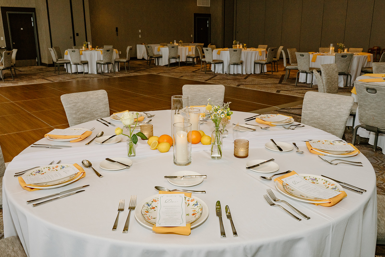 Round wedding reception table set with floral plates, citrus fruits, and glowing candles for a fresh and colorful PNW wedding vibe. 