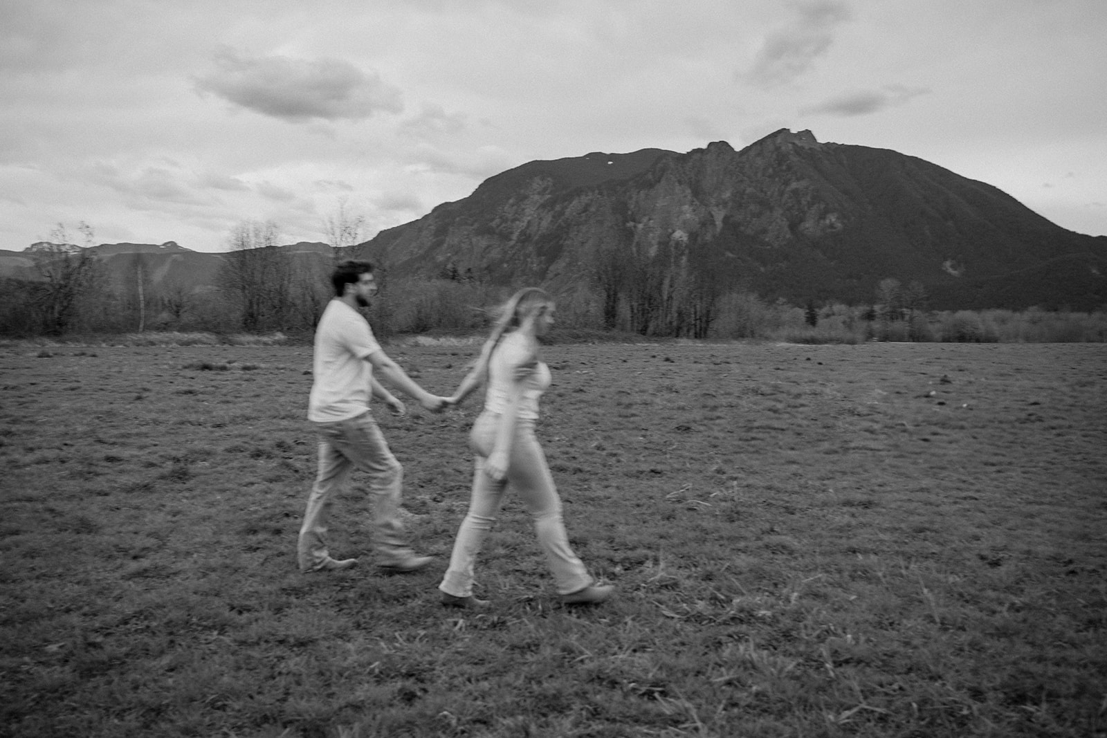 Couple walking hand in hand in front of a mountain range, showing off one of the best adventurous engagement photo locations in Washington