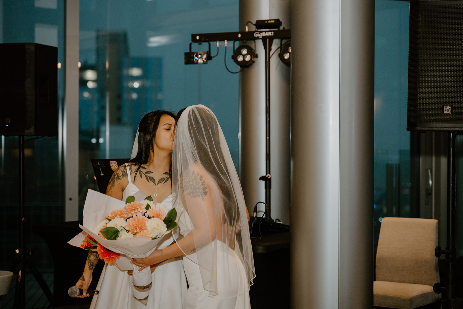 Brides kissing on the dance floor holding a microphone and their wedding bouqet