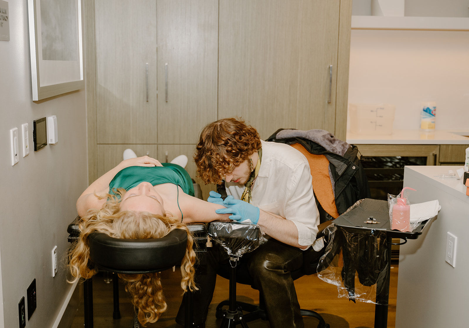 Tattoo artist at the after-party tattooing a guest on her arm while she's laying down.