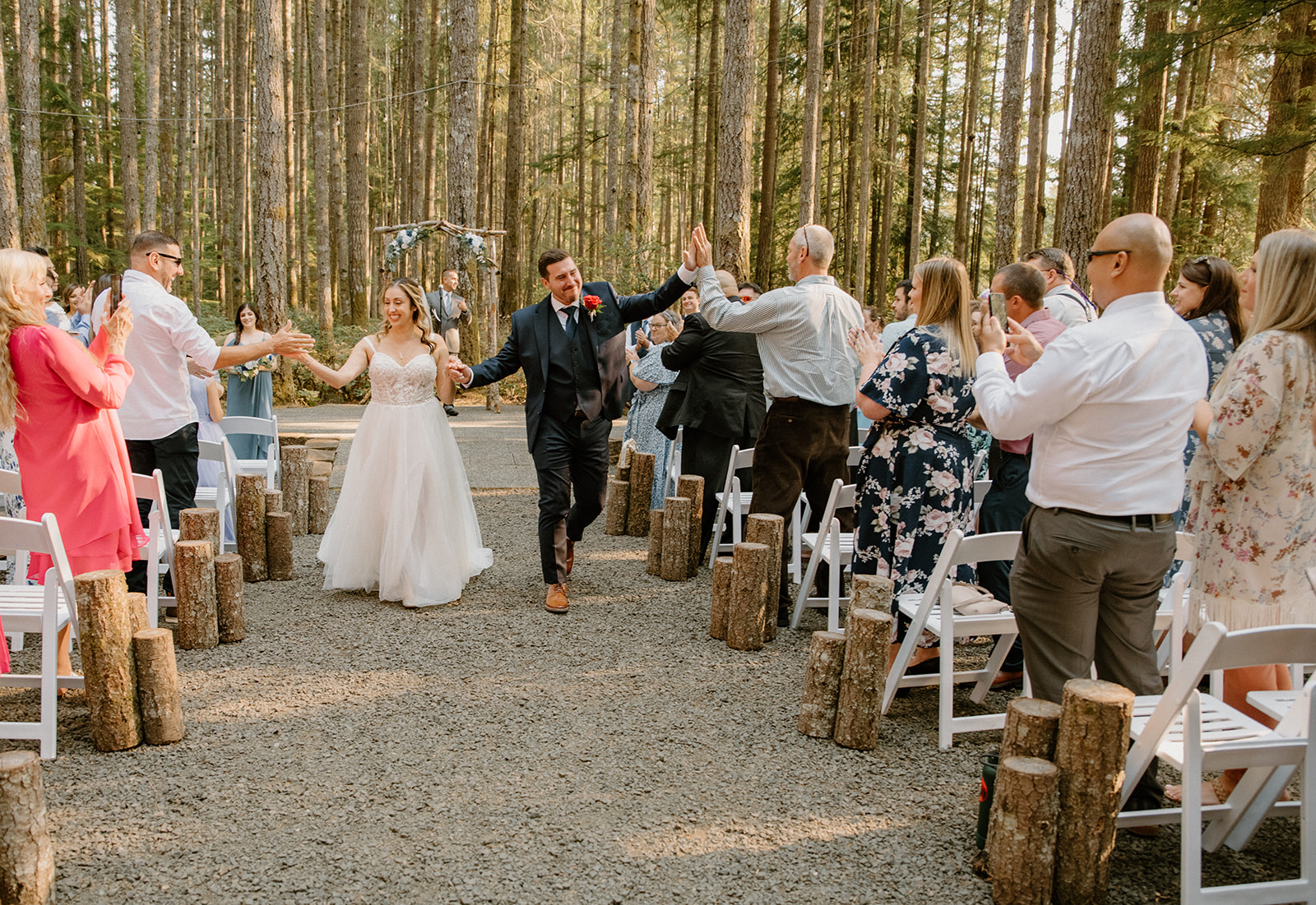 Newlyweds walk back down the aisle high-fiving guests in celebration—an unforgettable part of their joyful Pacific Northwest forest wedding.