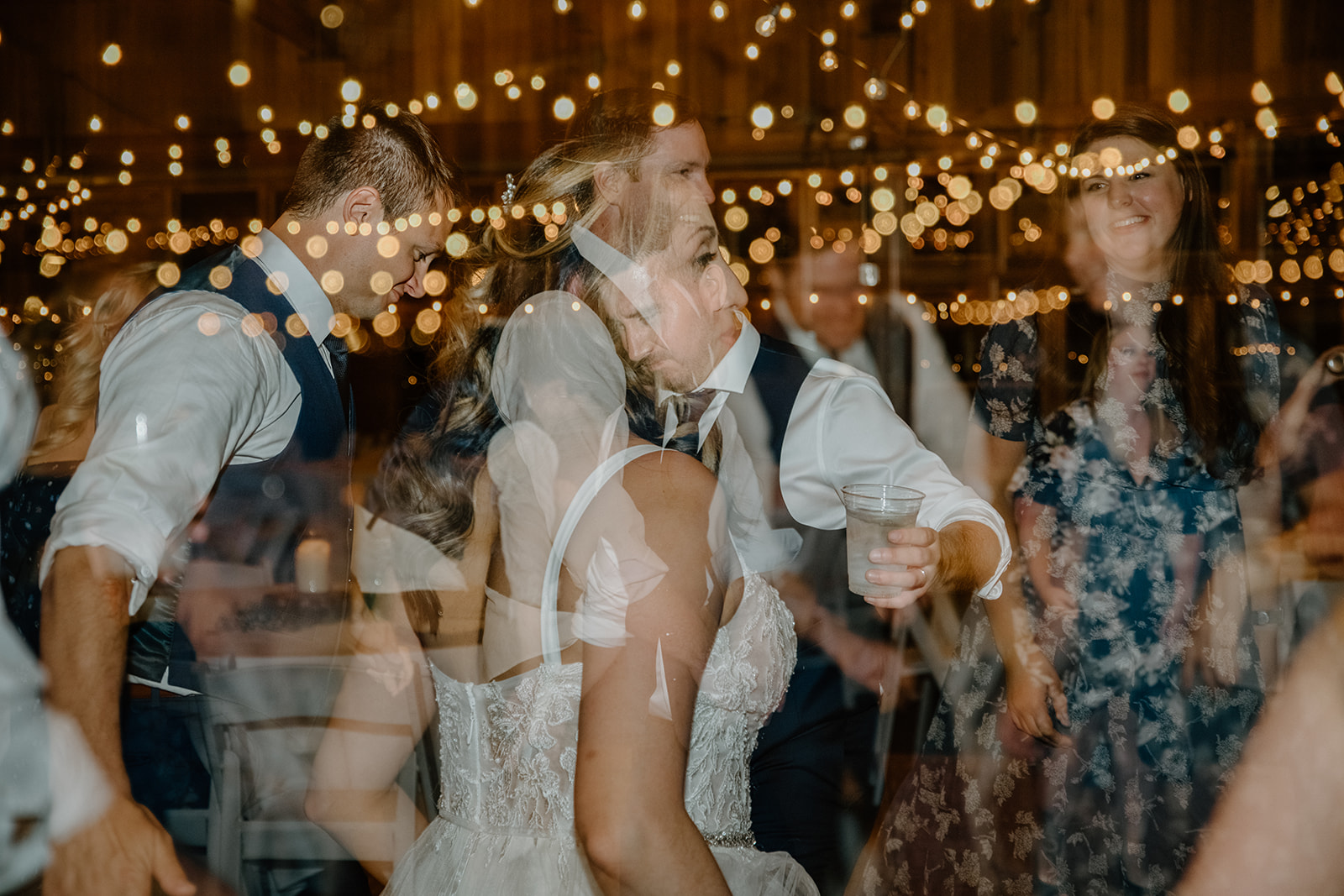 Double exposure photo of the bride and groom dancing surrounded by guests and twinkle lights, creating a dreamy celebration vibe. Pacific Northwest Wedding Planning Checklist.