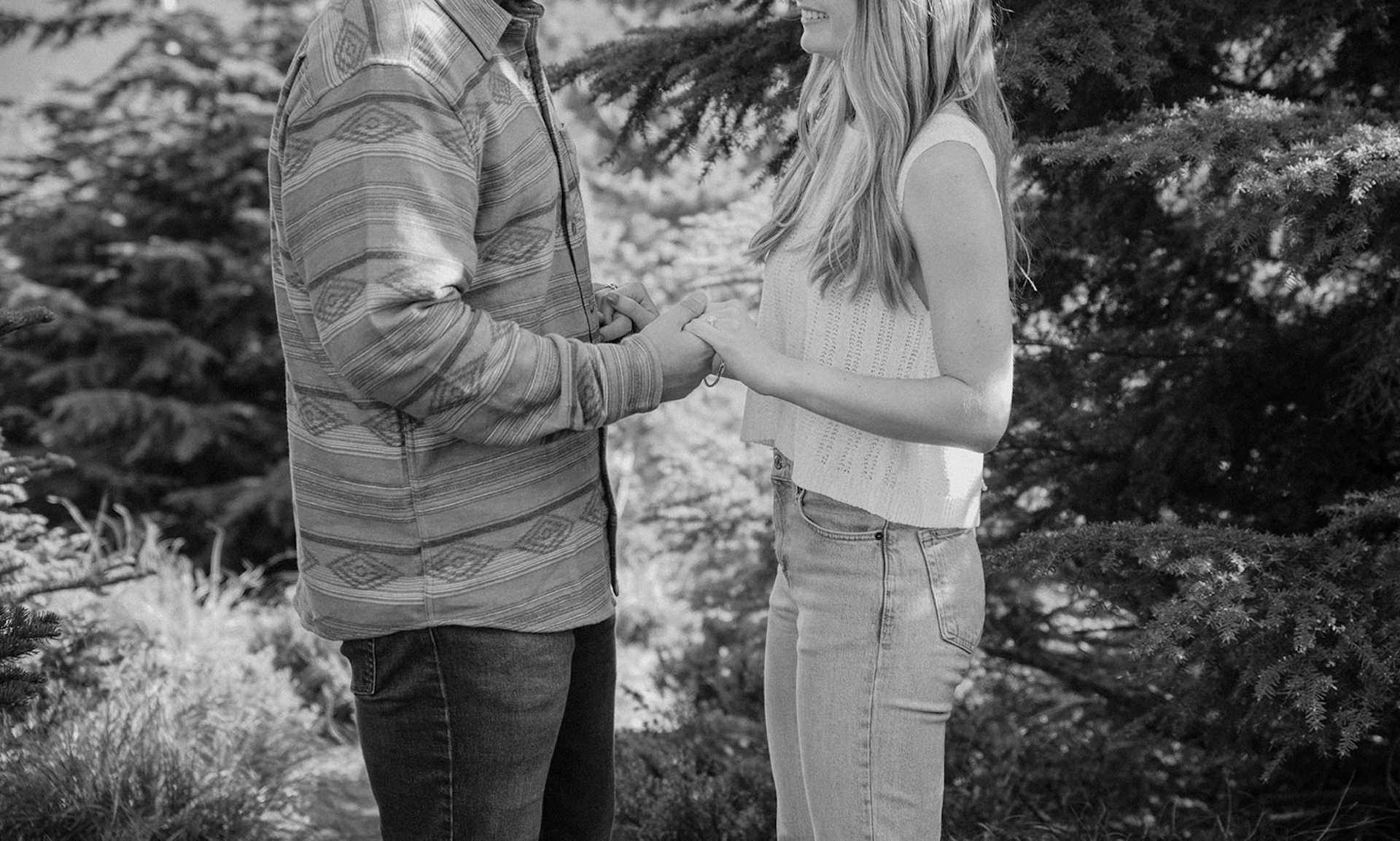 Black and white photo of a couple holding hands during an intimate engagement shoot in the forest. 