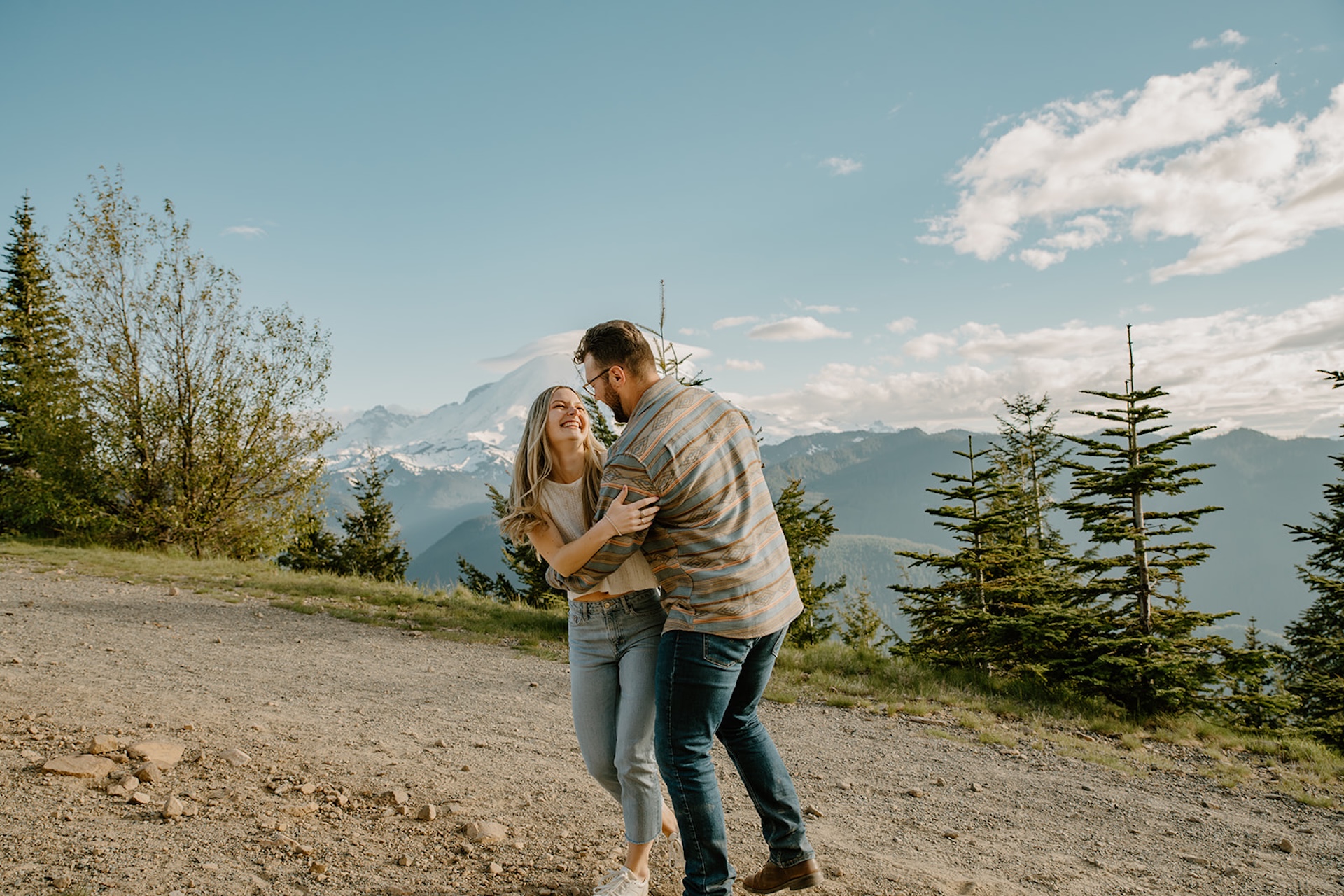 A couple laughing and playing together on a mountain road with Mount Rainier in the background. 