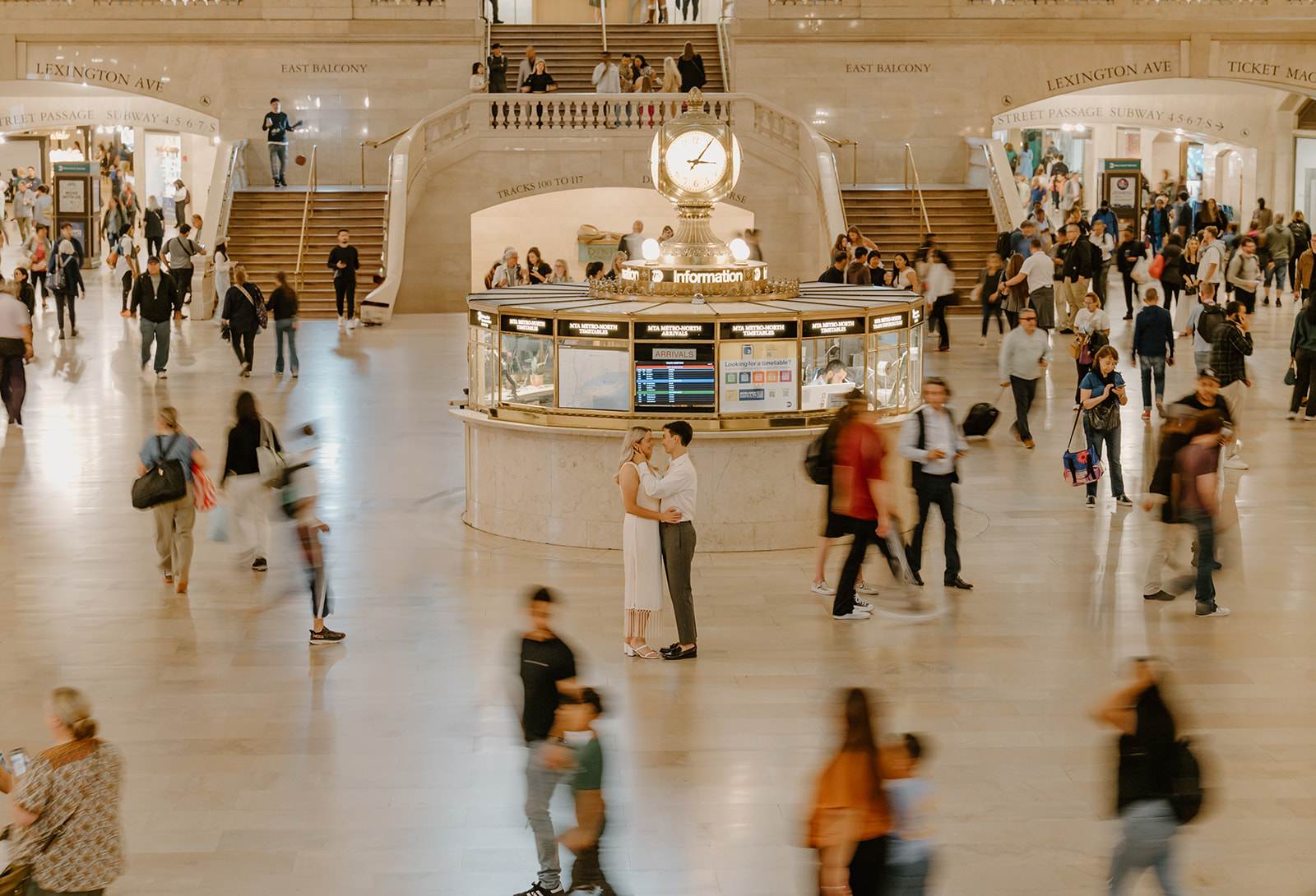 Motion blur photo of people walking in grand central station as the engaged couple is in focus in the middle of the chaos during their New York City Engagement photos