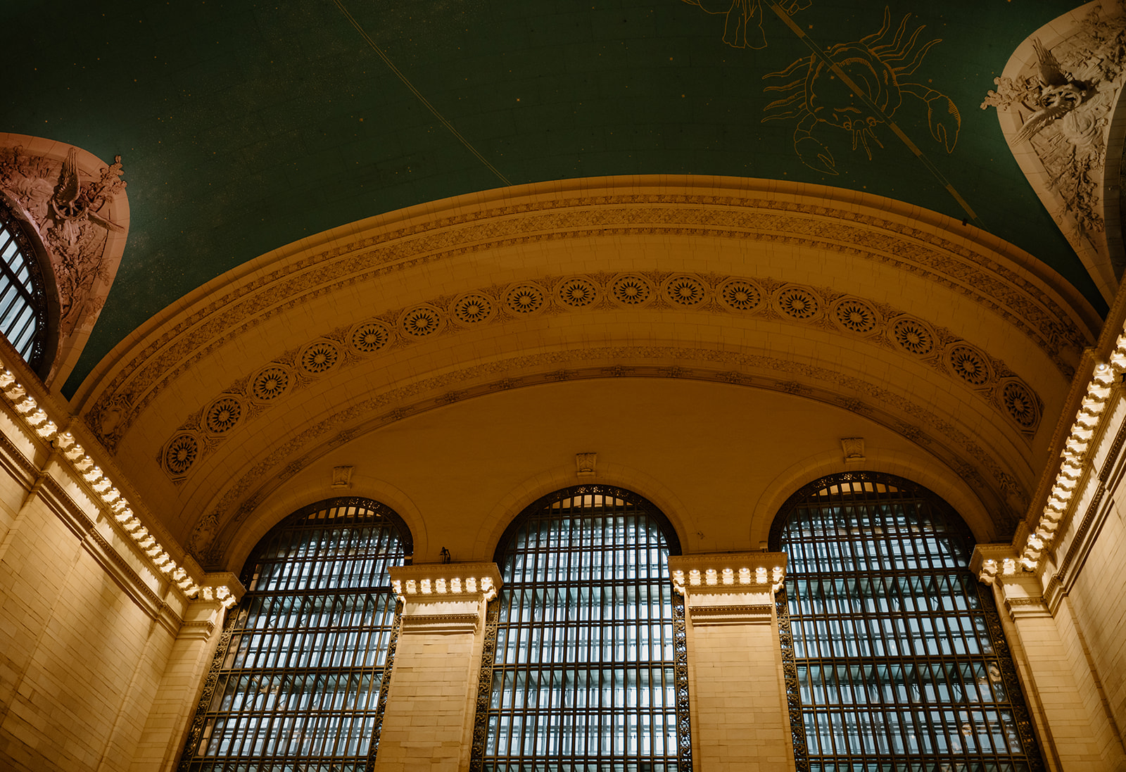 A gorgeous detail photo of the inside of the grand central station. It's the ceiling with deep green and gold tones.
