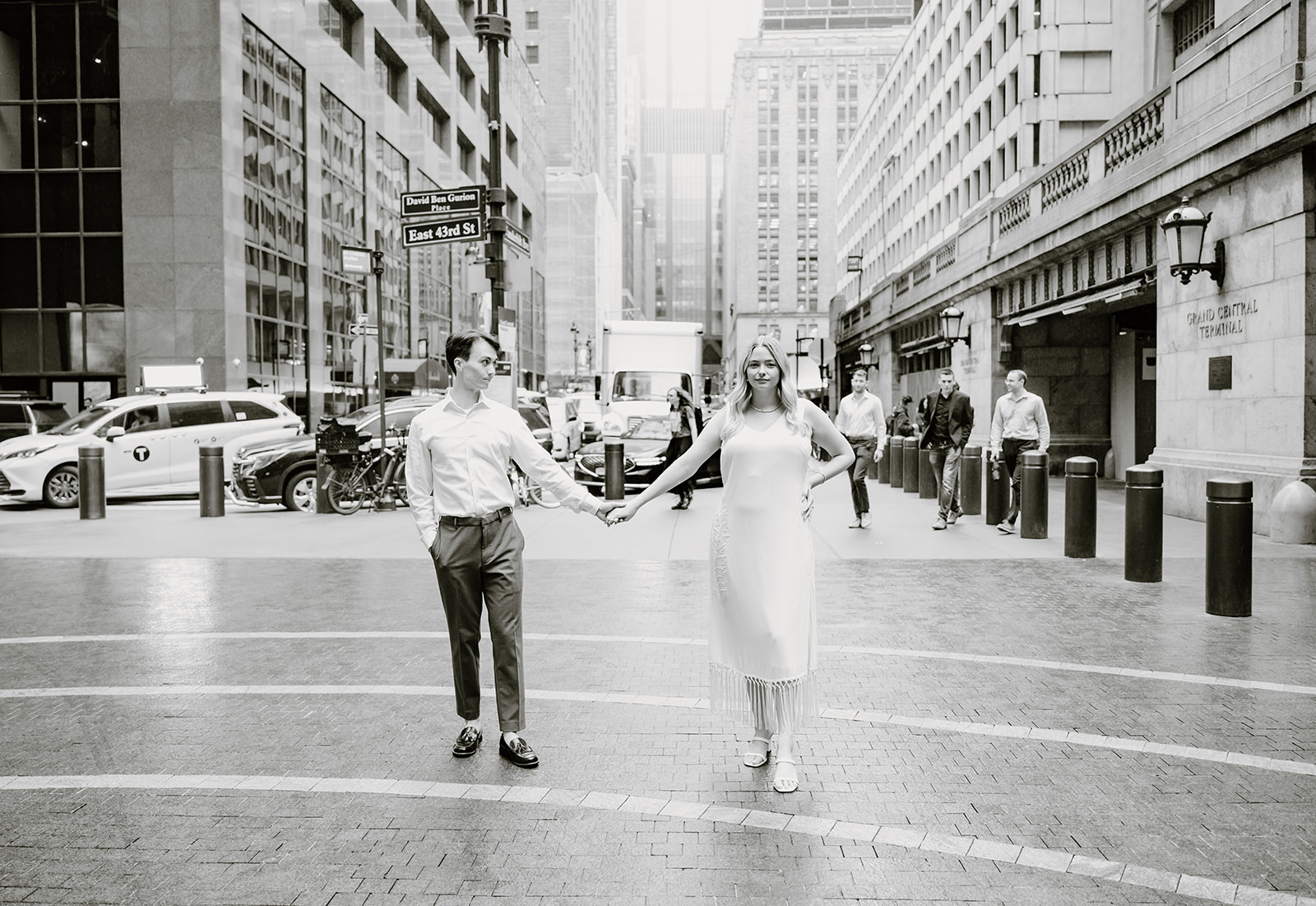 Couple holding hands and standing in the middle of the street smiling at each other with the city skyline behind them
