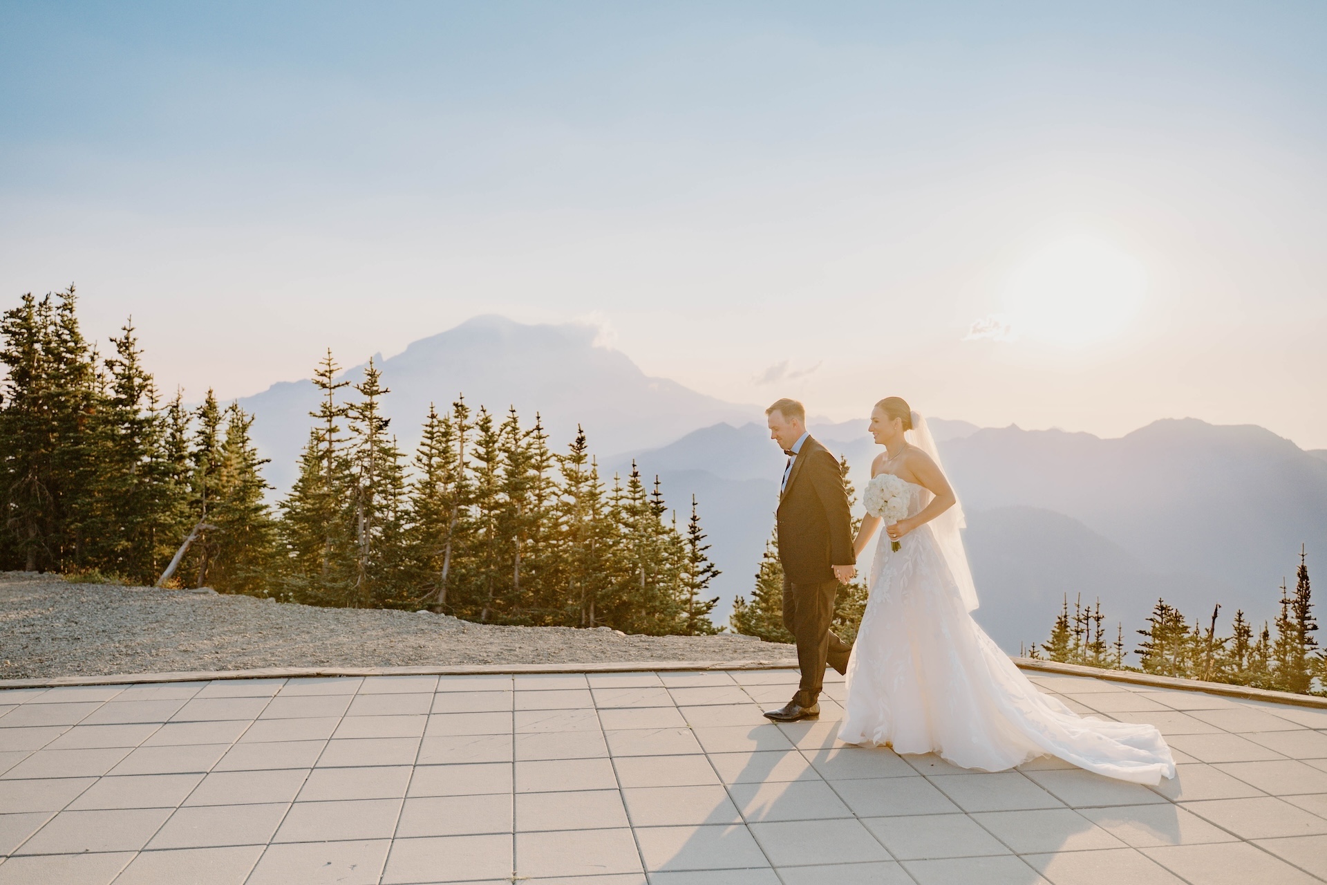 Bride and groom walking across an open patio at sunset with a glowing mountain peak behind them during a Crystal Mountain Resort Wedding.