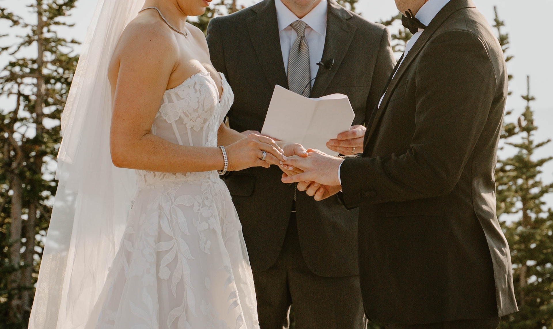 Close-up of the bride placing a ring on the groom’s finger during their outdoor ceremony.