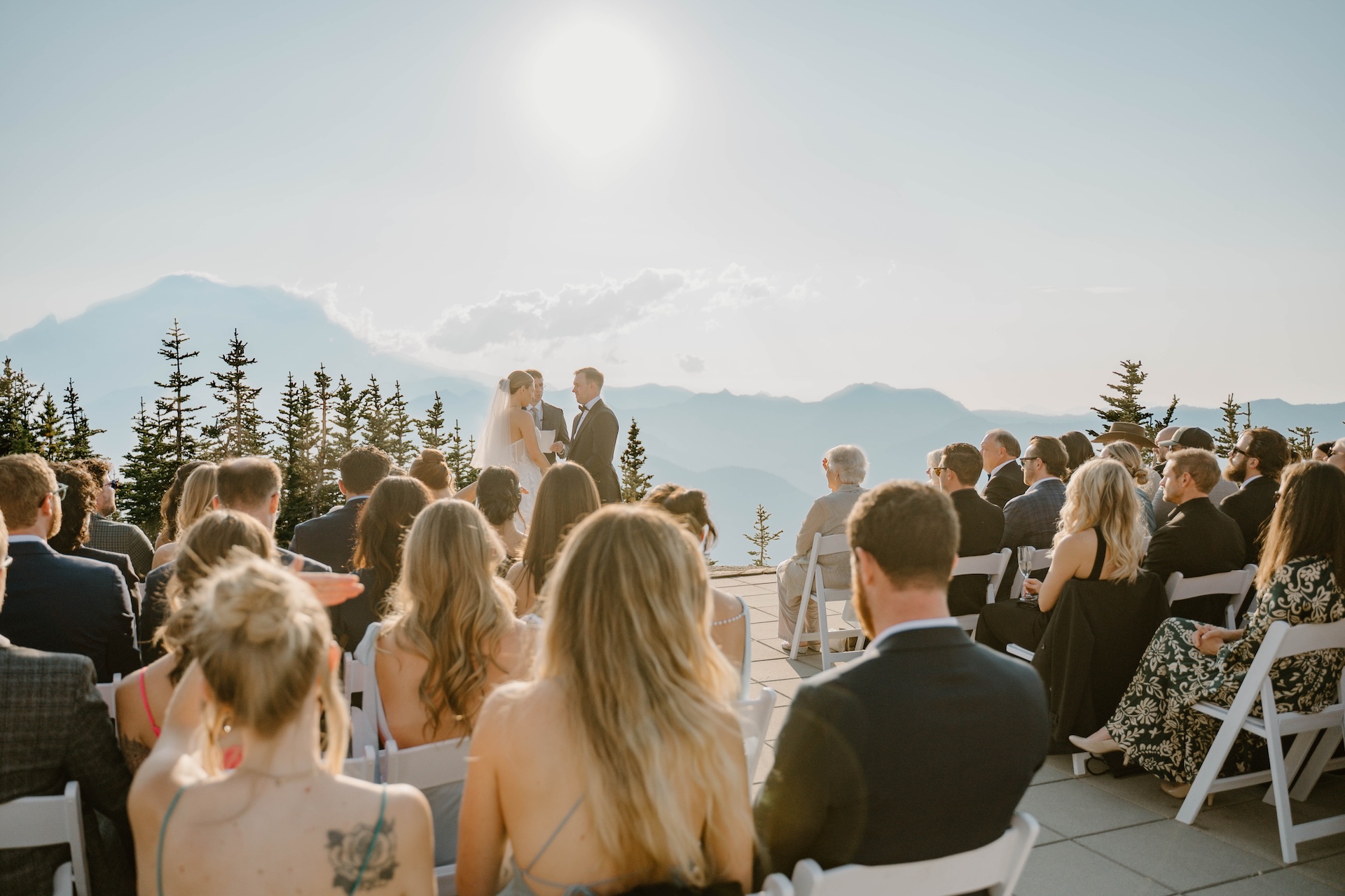 Wide view of the ceremony with guests seated outdoors facing the couple against mountain backdrops.