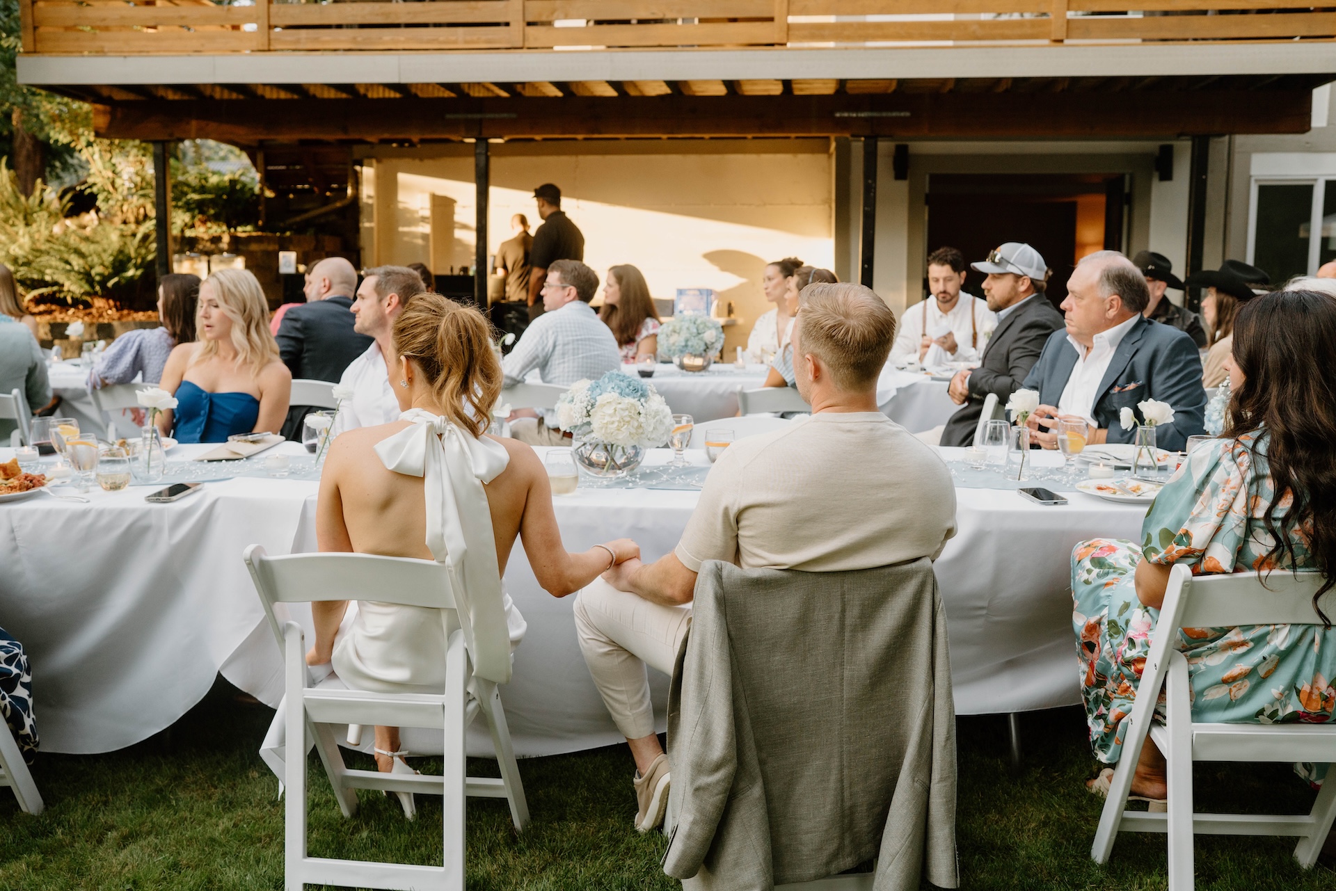 Guests seated at long white tables listening to toasts during a backyard Crystal Mountain Resort Wedding dinner.