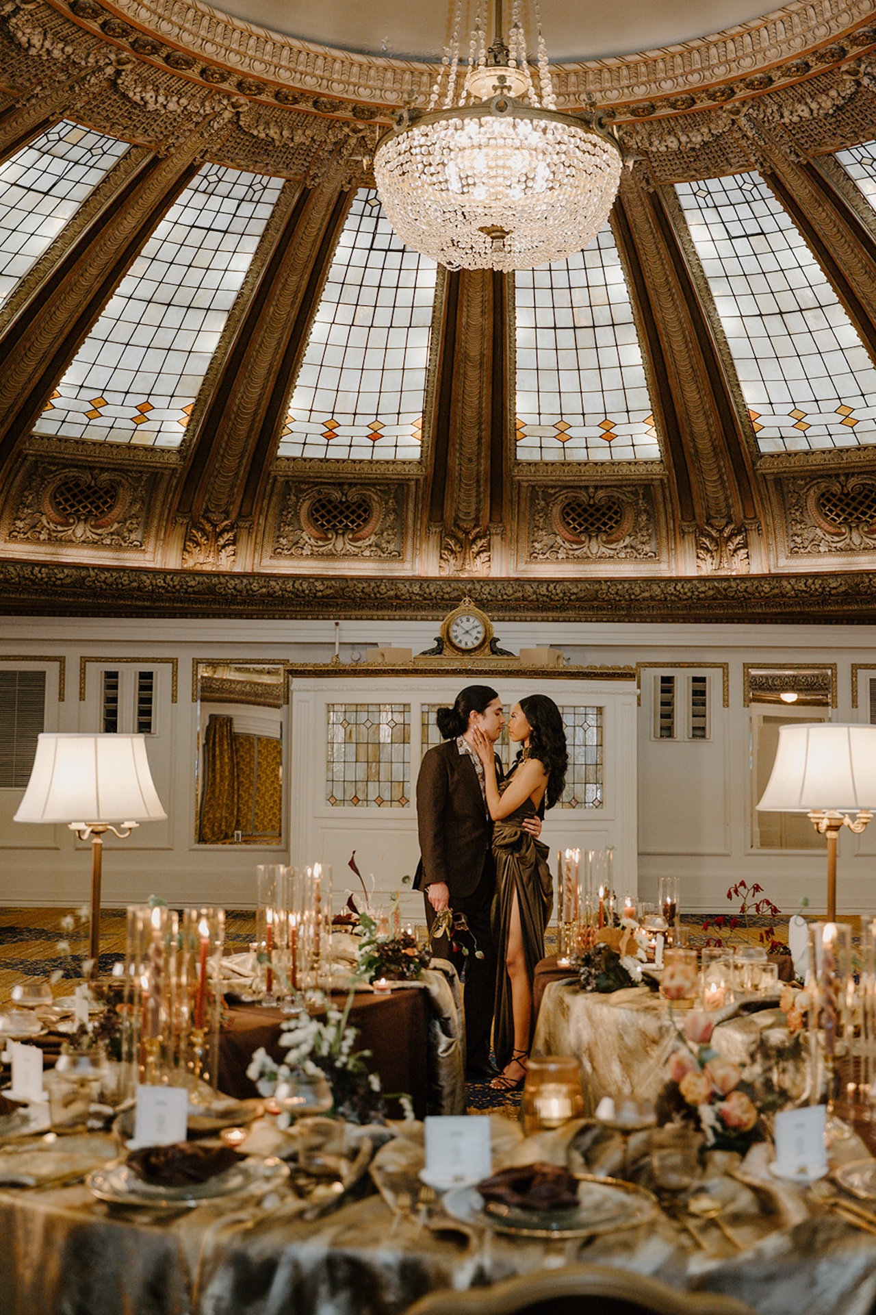 Couple kissing beneath a grand chandelier at their luxury wedding reception in an opulent ballroom.