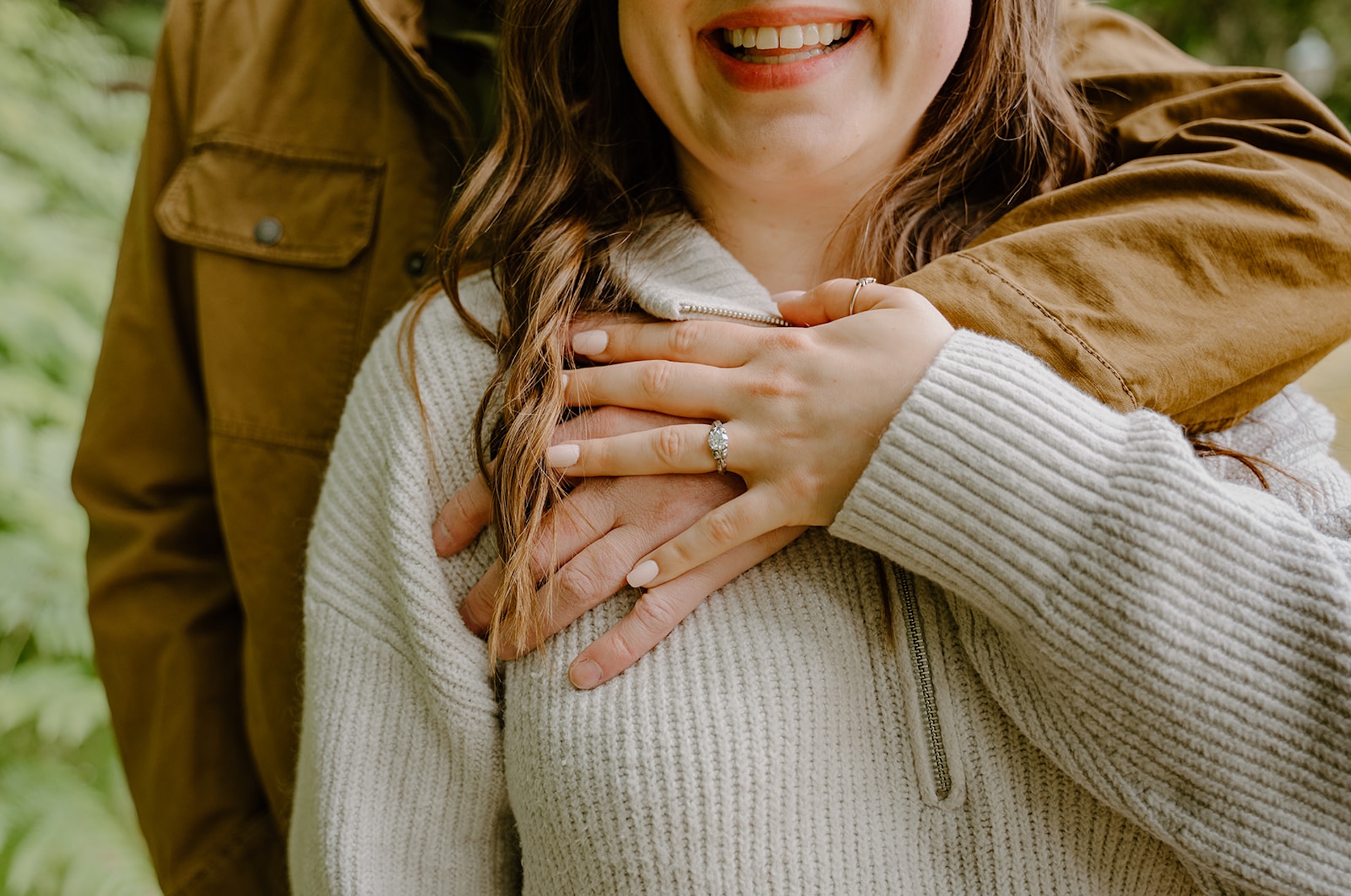 Close up image of the couples hand interlaced over her chest showing off her engagement ring.