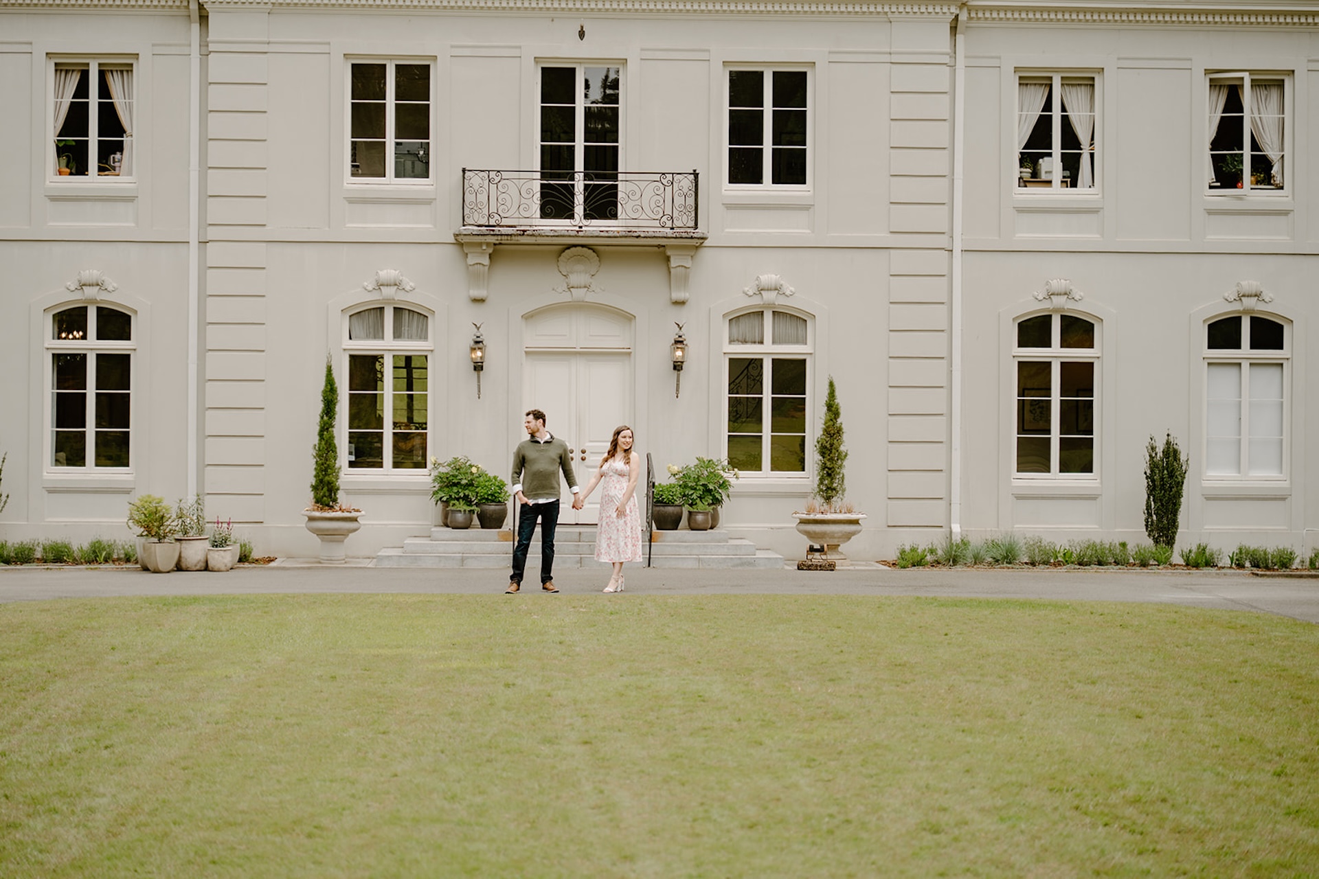Couple holding hands and looking away from each other in front of a historic white building at Bloedel Reserve in Washington during their engagement shoot.