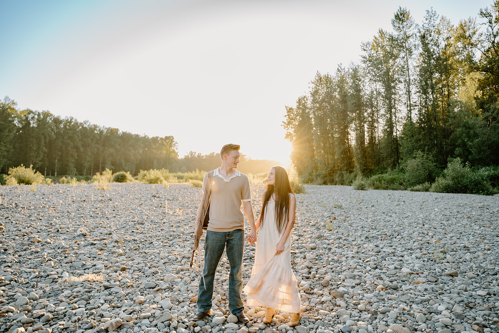 They walk hand-in-hand across the rocky riverbed with sunlight flaring behind them, demonstrating natural ease in When to take engagement photos.