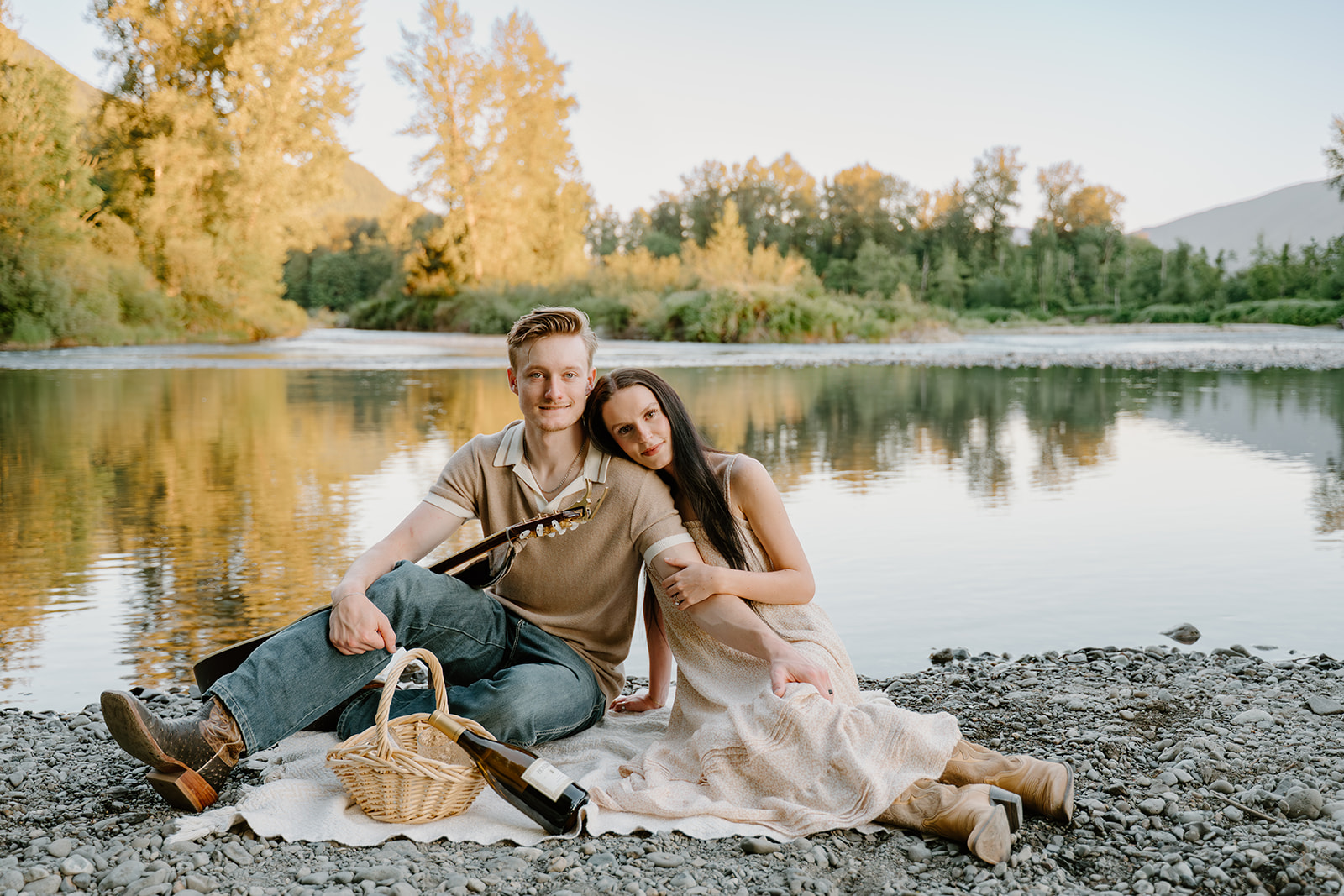 The couple sits close together on a blanket with a guitar and picnic basket beside them, a relaxed scene perfect for When to take engagement photos.