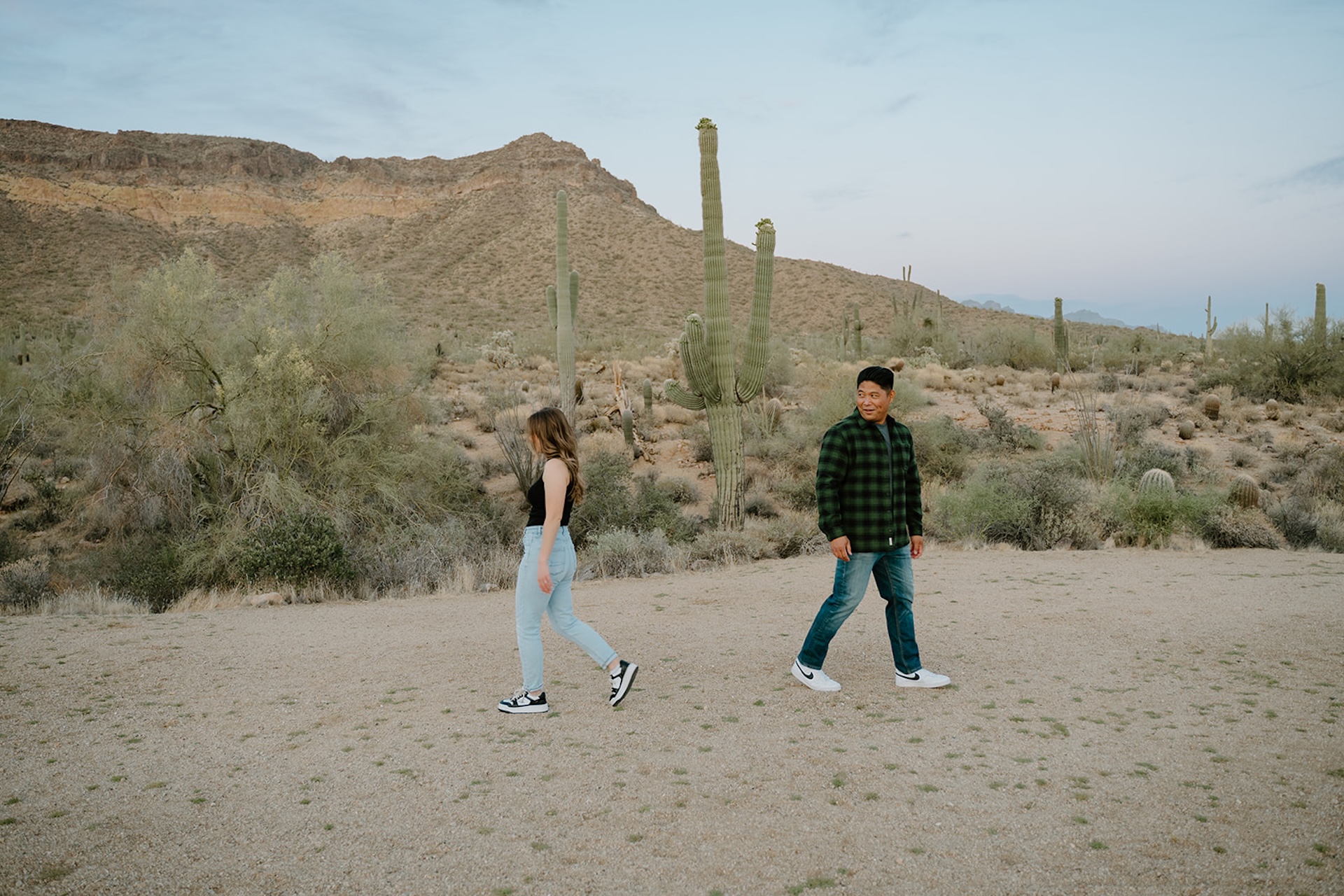 A playful photo of an engaged couple walking away from each other across a desert landscape, creating movement and space between them.