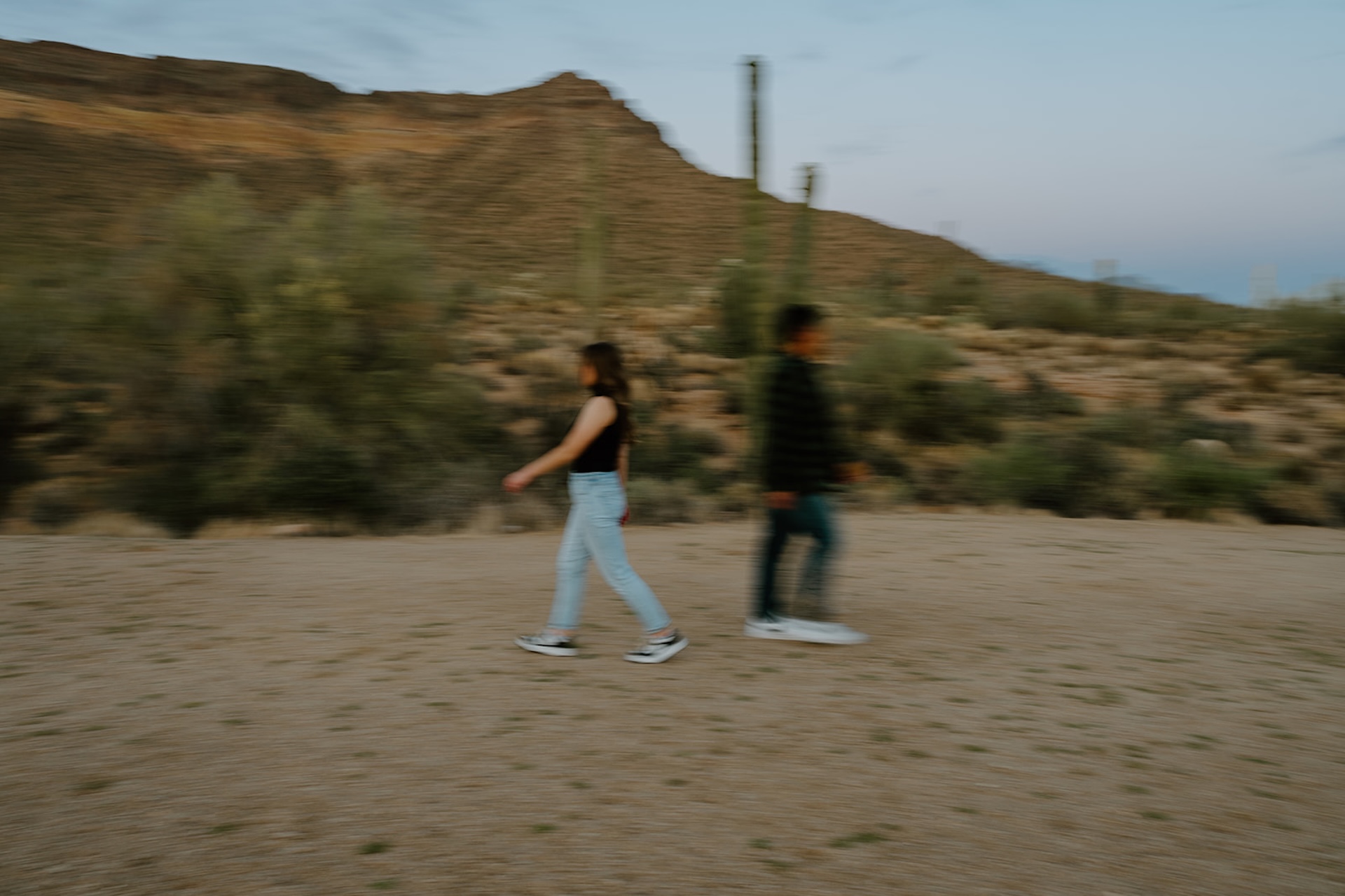 A motion-blur photo of the couple walking in opposite directions across a desert clearing, adding movement and creativity to arizona engagement photos.
