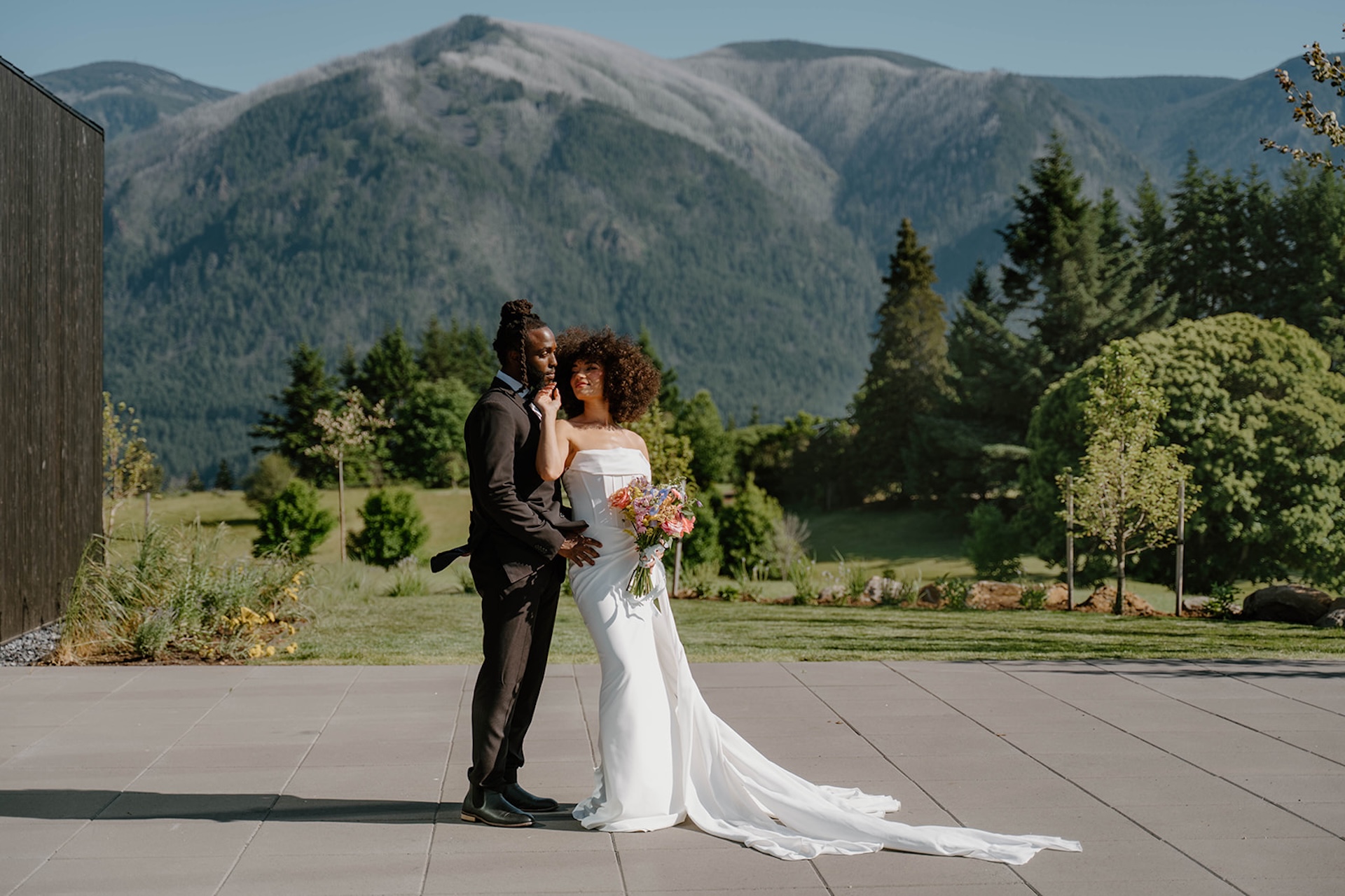 Bride and groom standing together on a modern patio during a wind mountain ranch wedding, with sweeping mountain views and greenery surrounding them.